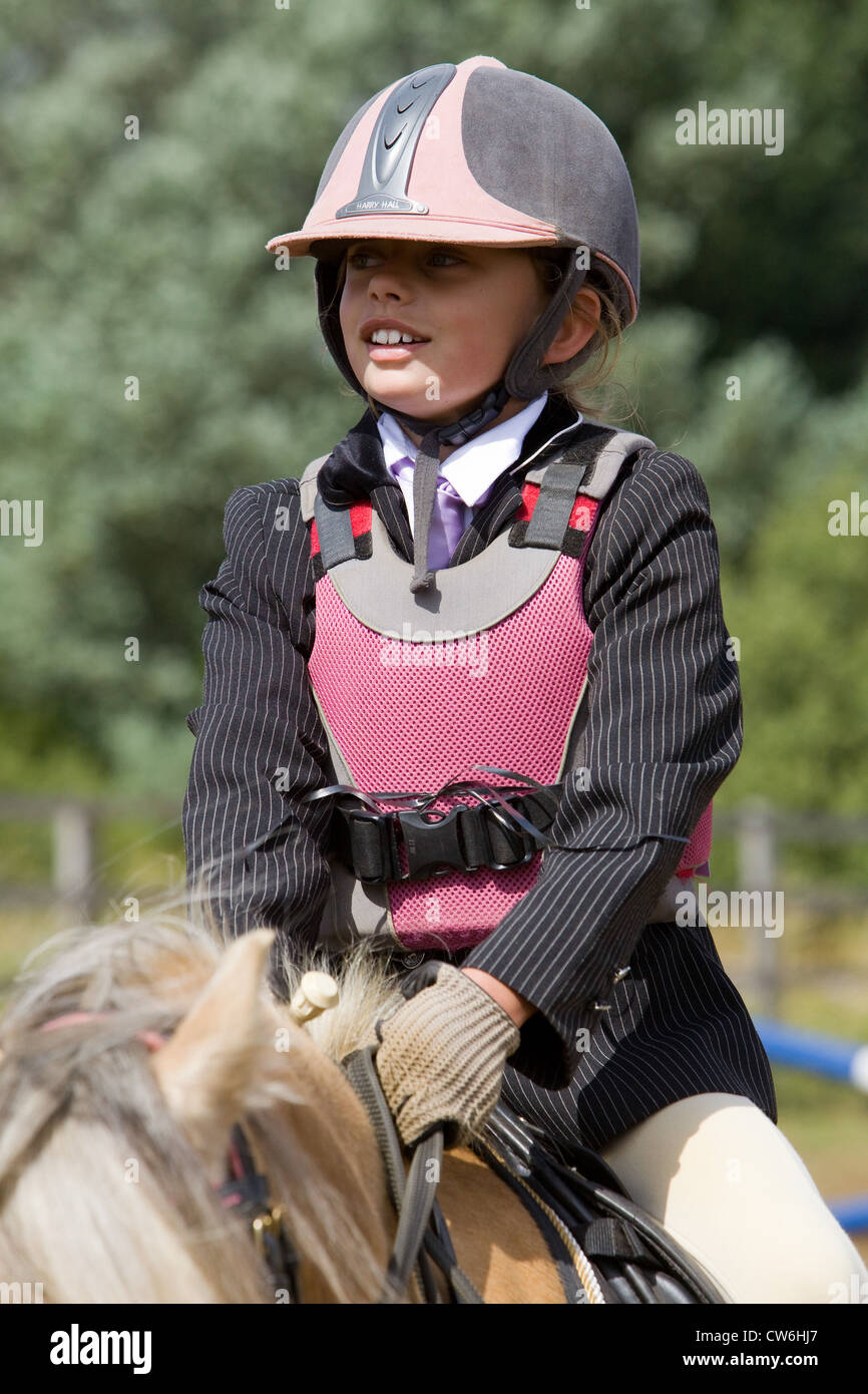 Una giovane ragazza di indossare un equipaggiamento di sicurezza e abbigliamento durante la seduta sul suo pony Foto Stock