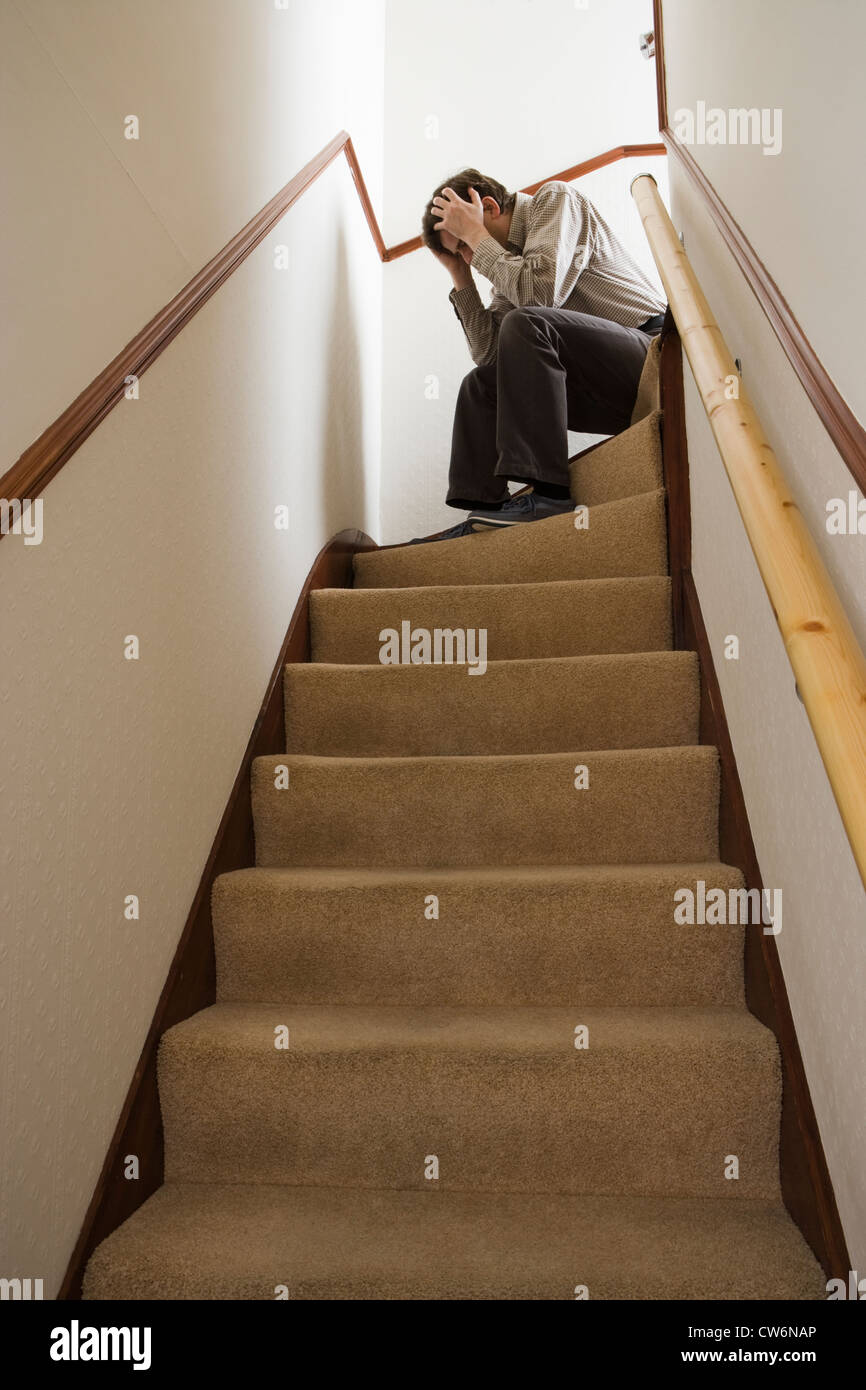 Uomo seduto sulle scale, testa in mani. Foto Stock