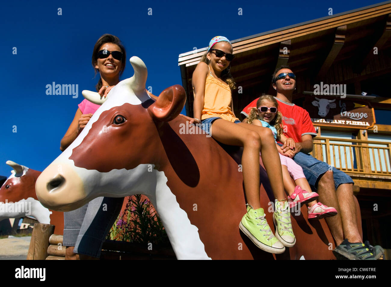 Famiglia giovane con due ragazze divertirsi seduti su una vita dimensioni mucca di plastica in una località di montagna, Francia, Savoie, Alpi Foto Stock