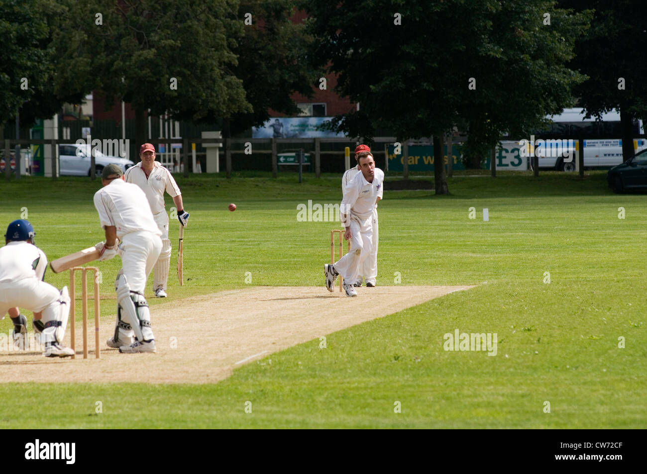 Partita di cricket village green gioca a giocare i giocatori bat battitore bowler wicketkeeper paletto wickets verde prato inglese uk team fiel Foto Stock