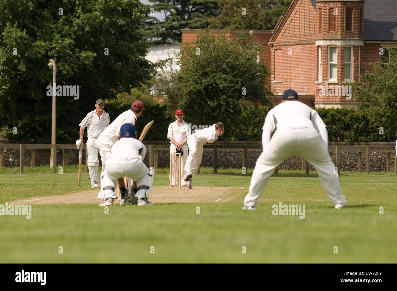 Partita di cricket village green gioca a giocare i giocatori bat battitore bowler wicketkeeper paletto wickets verde prato inglese uk team fiel Foto Stock