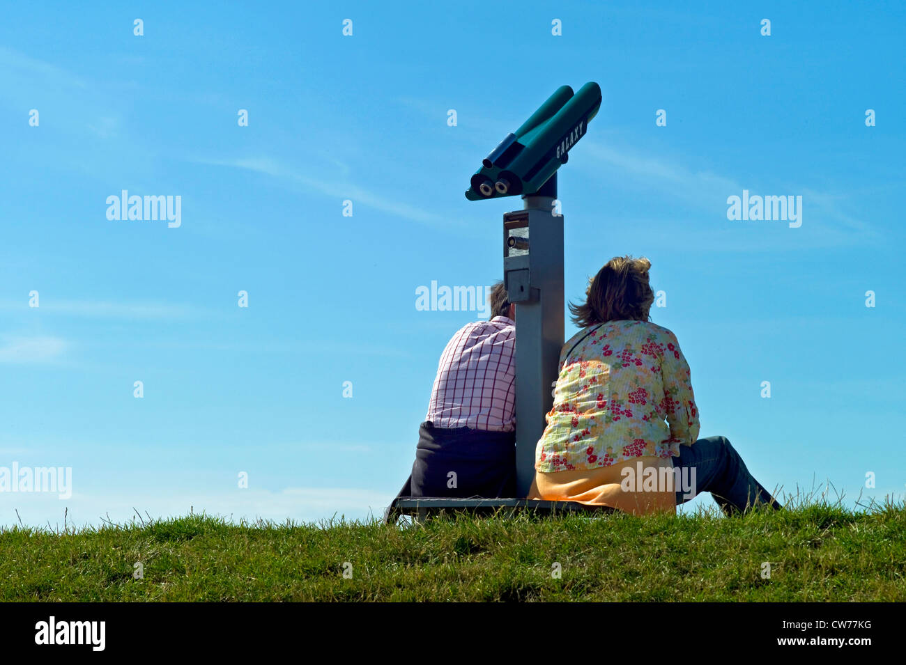 Due persone seduto accanto coin telescopio sulla dyke, Germania, Bassa Sassonia, Neuharlingersiel Foto Stock