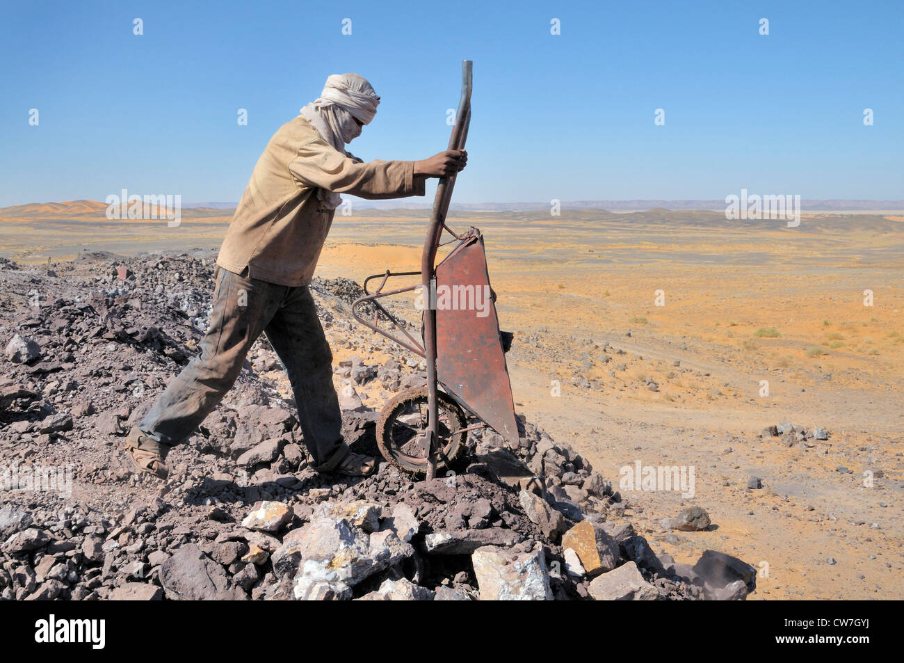 Dumping lavoratore una carriola di massi, miniere di solfuro di piombo , Marocco, Erg Chebbi Foto Stock