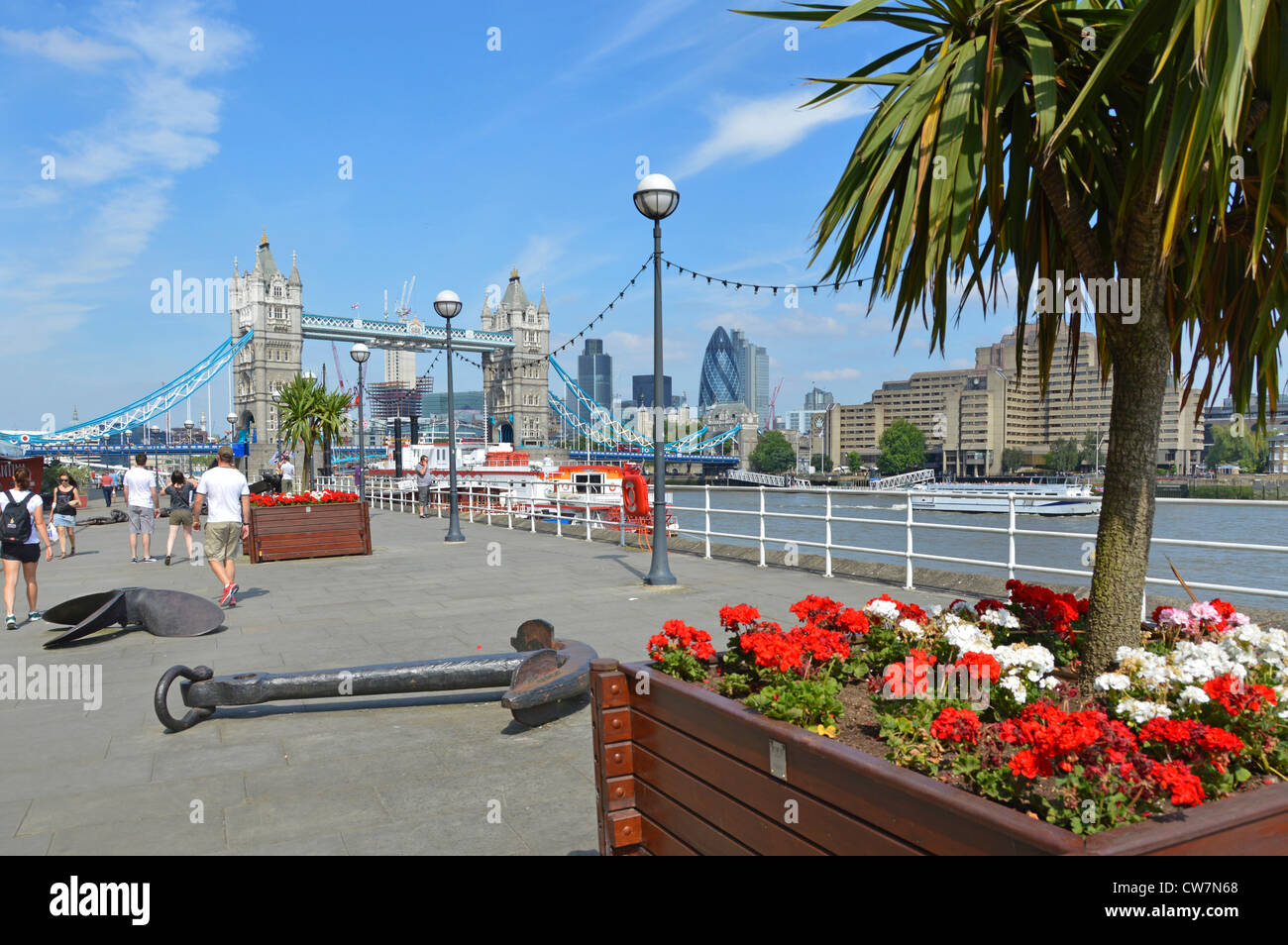 Percorso del Tamigi Butlers Wharf sul fiume Tamigi vedute del Tower Bridge e dello skyline di Londra fiori sul lato dell'acqua in scatole di piantatrice e alberi di cordyline Londra Regno Unito Foto Stock
