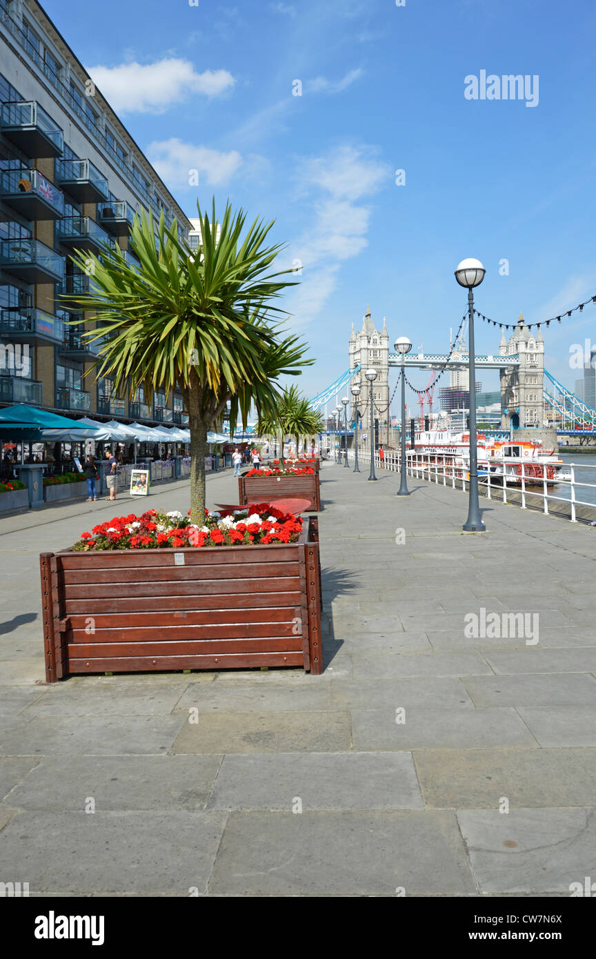 Thames Path Butlers Wharf on River Thames Tower Bridge view River side Apartments ristoranti canopie & red flower cordyline tree planters London UK Foto Stock