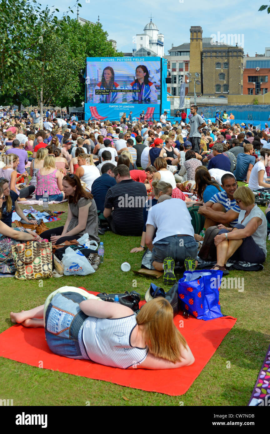 La folla di persone si siede sull'erba guardando le Olimpiadi di Londra del 2012 TV sport evento grande schermo televisivo esterno in Potters Fields Park Southwark Inghilterra Regno Unito Foto Stock