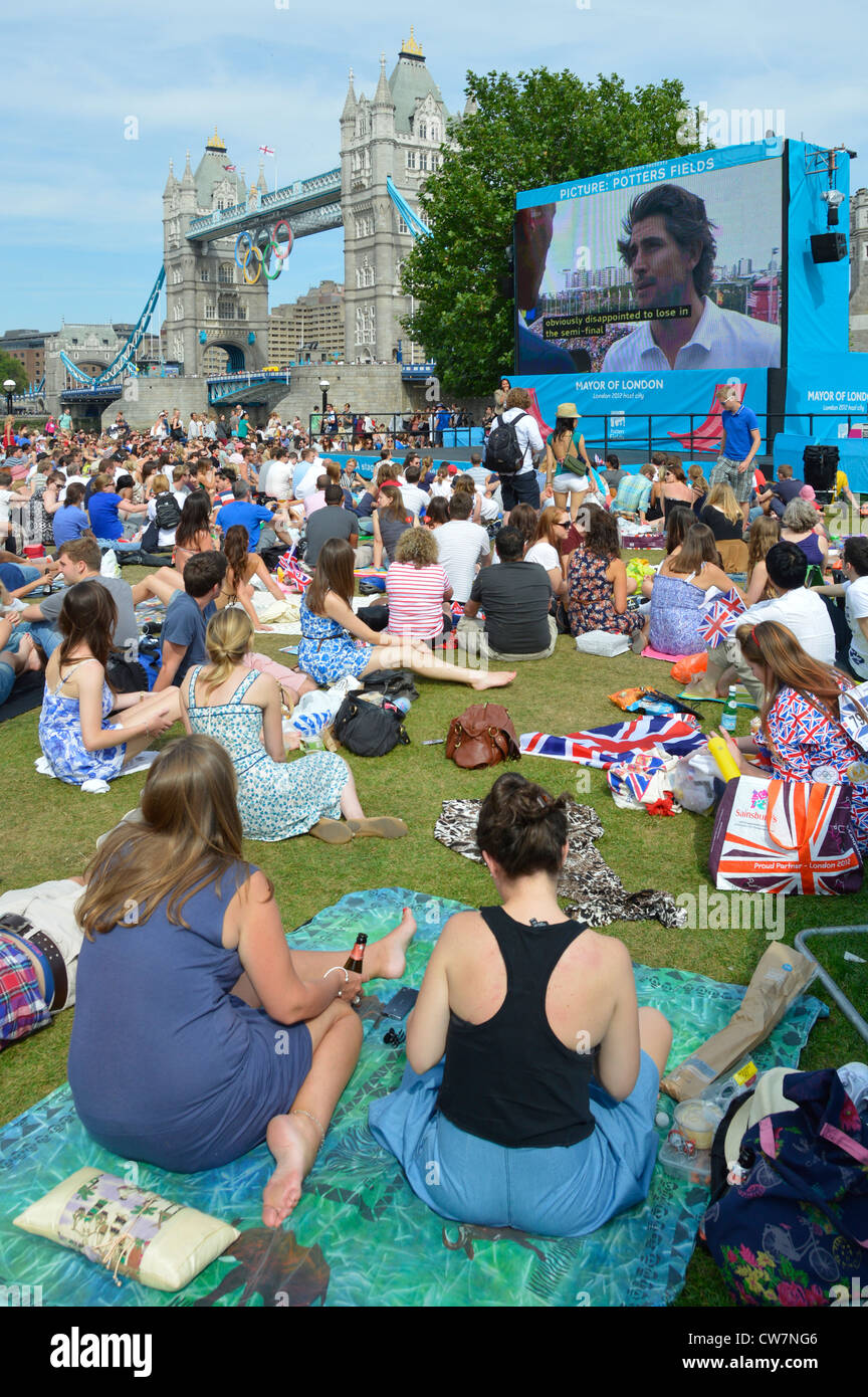 La folla di persone si siede sull'erba guardando le Olimpiadi di Londra del 2012 TV sport evento grande schermo televisivo esterno in Potters Fields Park Southwark Inghilterra Regno Unito Foto Stock