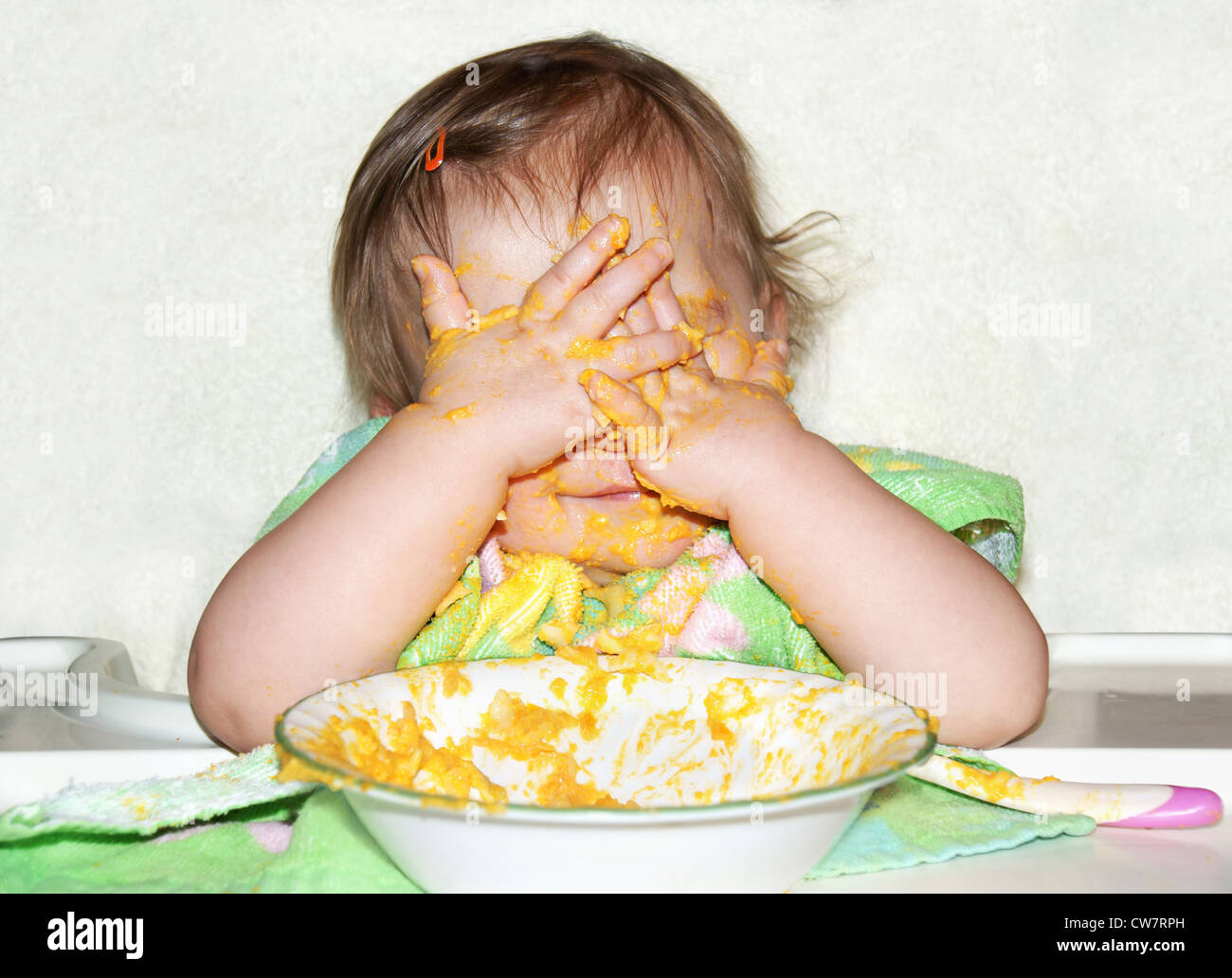 Funny baby con cibo volto coperto da mettere le mani sui suoi occhi per riprodurre picaboo durante il pasto, momento sbagliato a farlo. Foto Stock