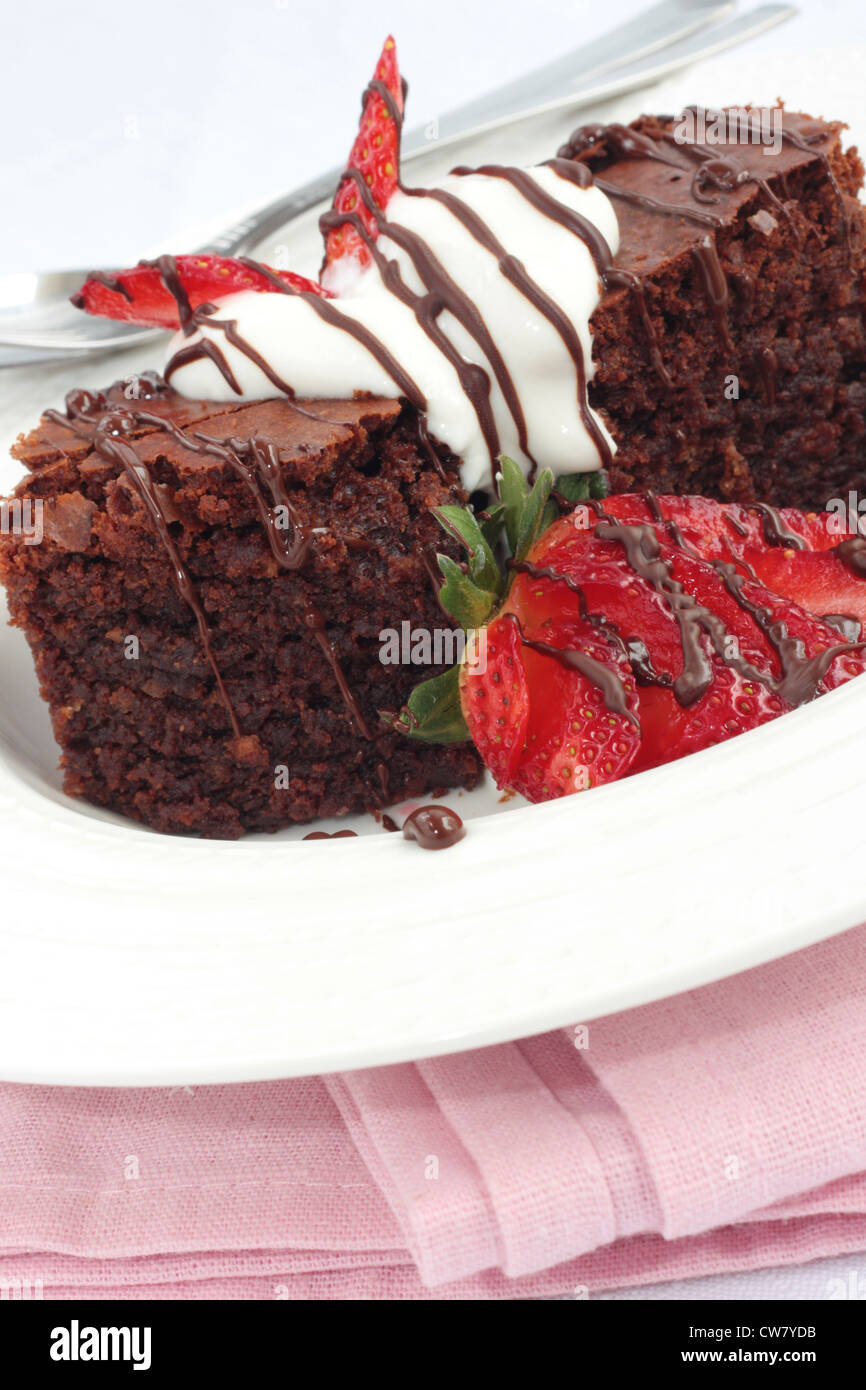 Brownie al cioccolato con panna e fragole. Su uno sfondo di colore rosa. Foto Stock