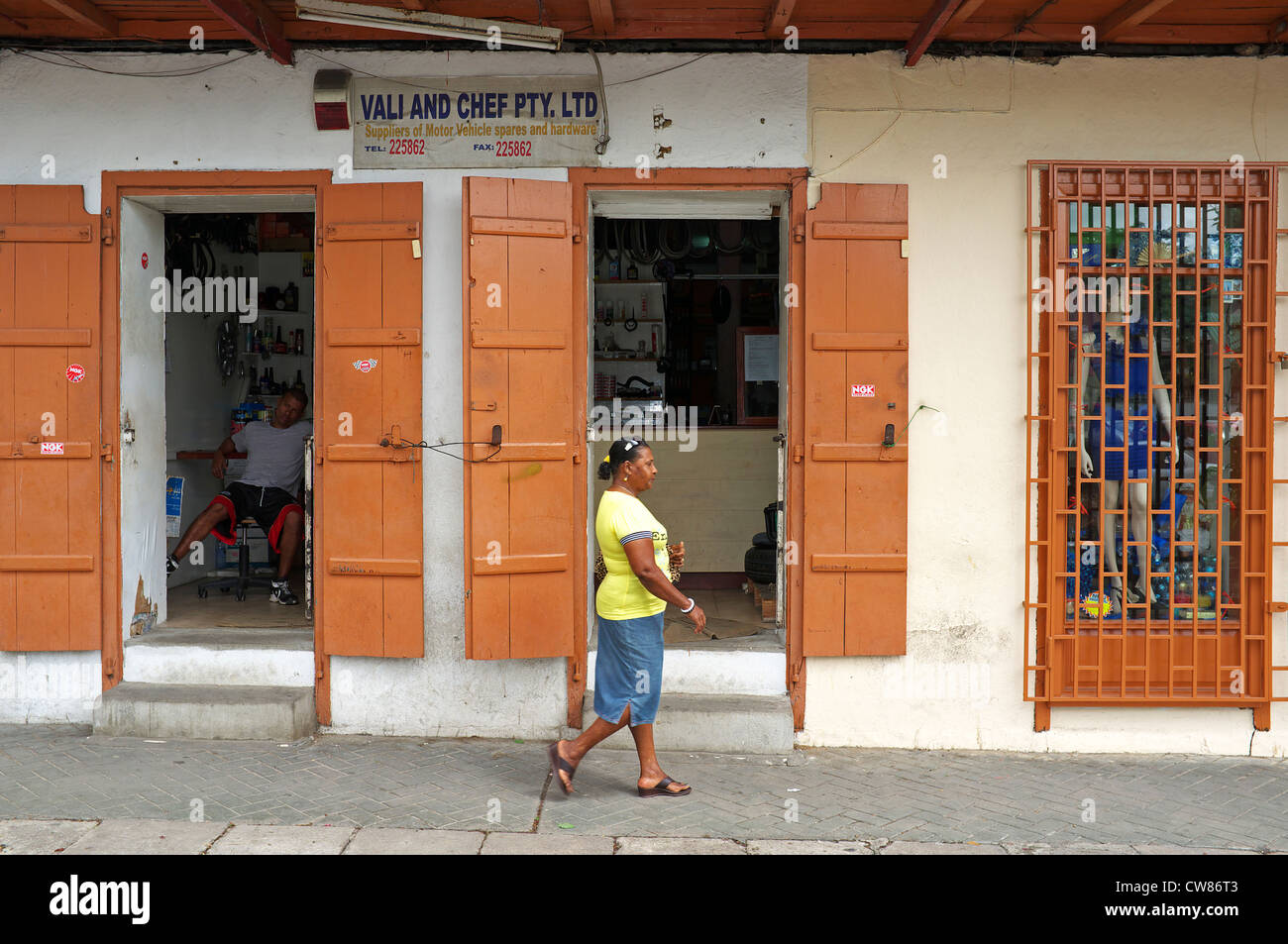 Scena di strada con un motore negozio per pezzi di ricambio e di una donna a piedi da Victoria, Isola di Mahe, Seicelle Foto Stock