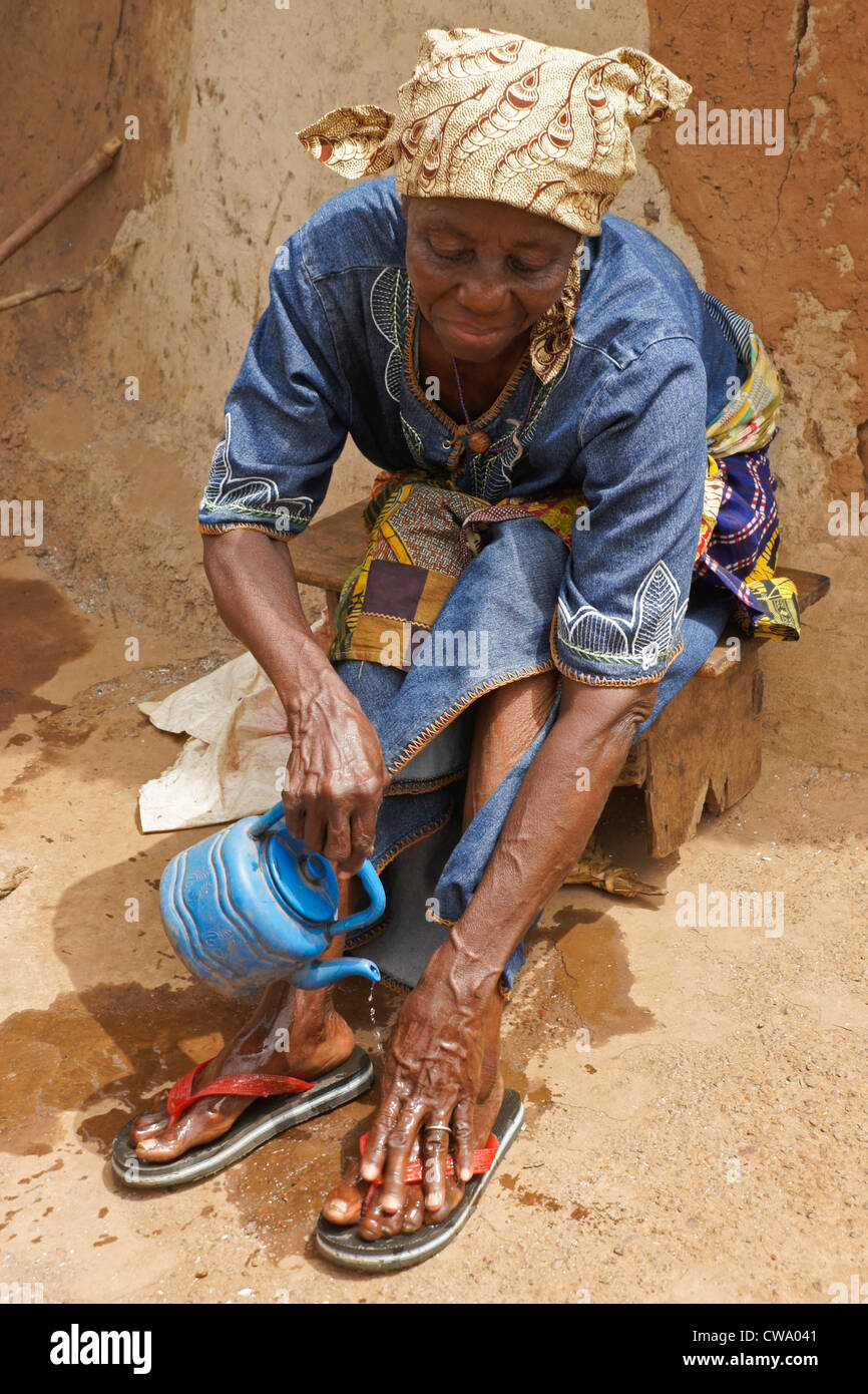 Donna lavando i suoi piedi fuori capanna di fango, Gambaga, Ghana Foto Stock