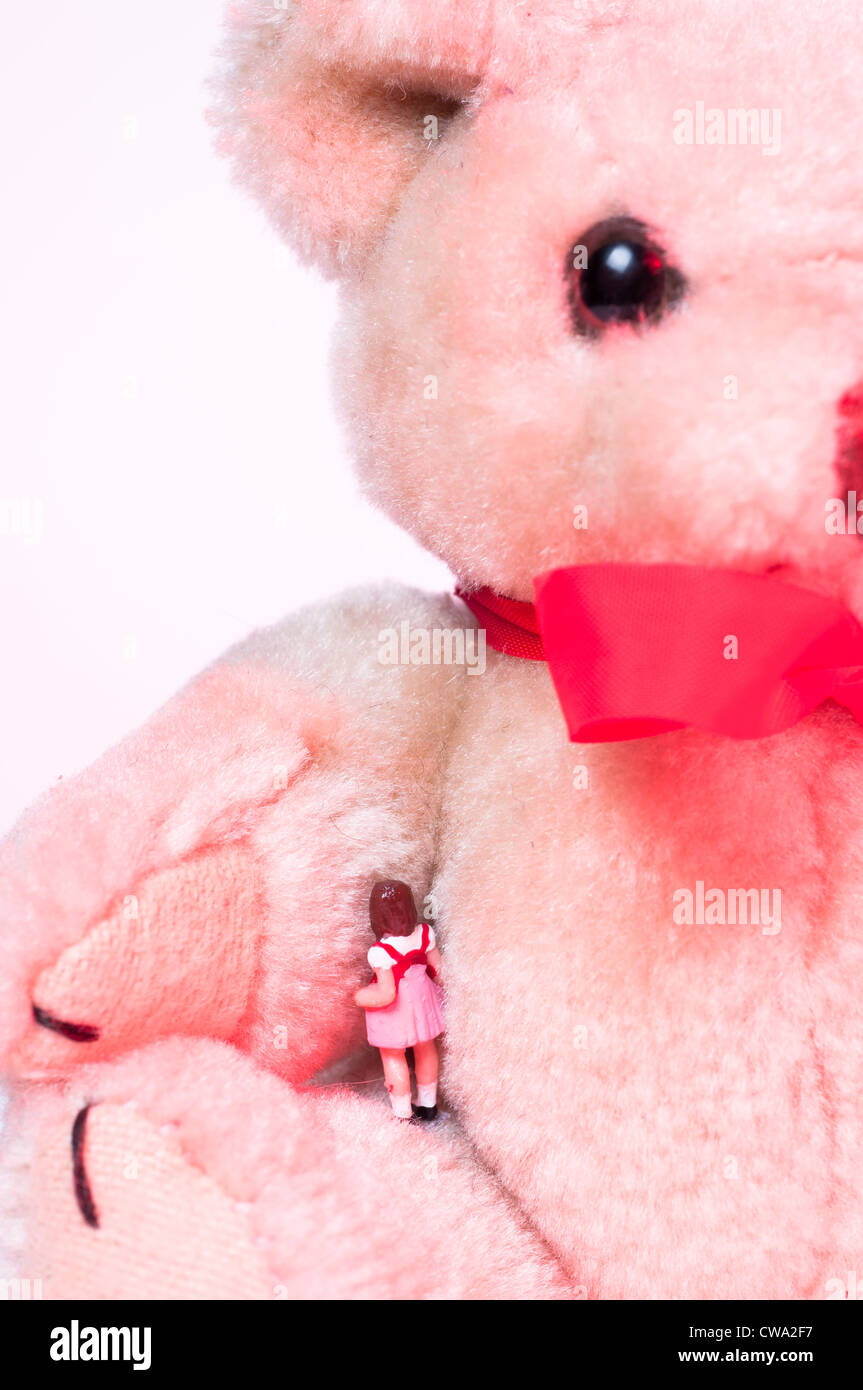 Piccola ragazza giocattolo in piedi sotto il Teddy bear's arm Foto Stock