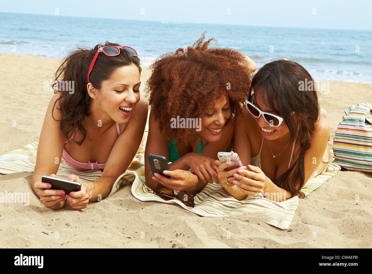 Giovani donne sulla spiaggia con i telefoni cellulari Foto Stock