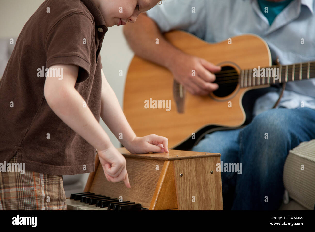 Ragazzo giocando Little pianoforte come uomo suona la chitarra Foto Stock