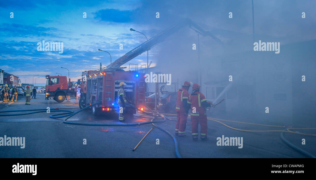 I Vigili del Fuoco in azione la spruzzatura di fiamme.Riparazione Auto negozio il fuoco nel sobborgo di Reykjavik, Islanda Foto Stock