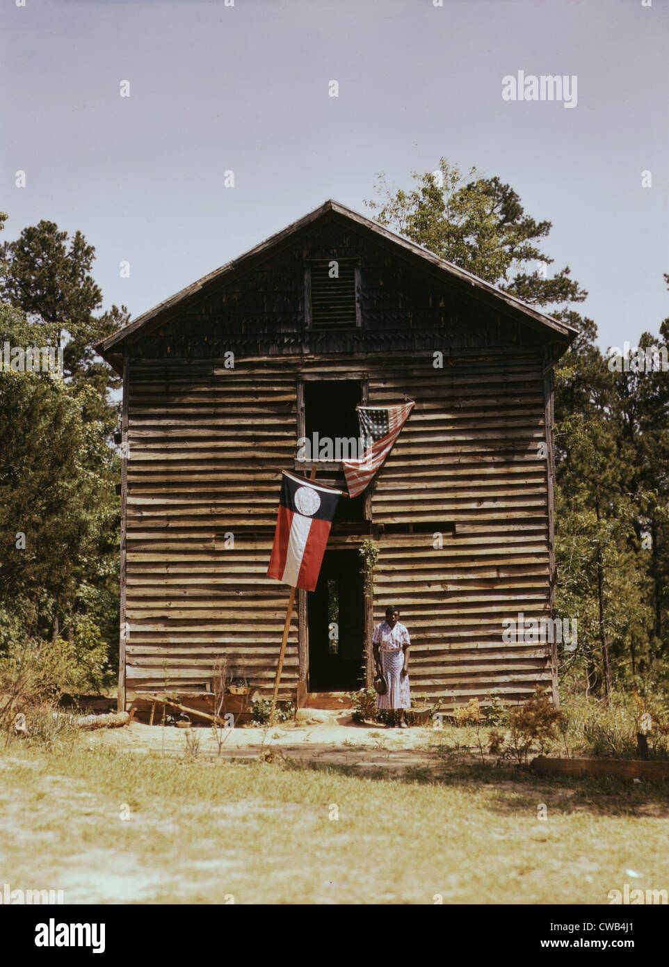 African American woman standing da edificio con lo stato della Georgia e Stati Uniti bandiere, vicino a White Plains, Georgia, fotografia Foto Stock