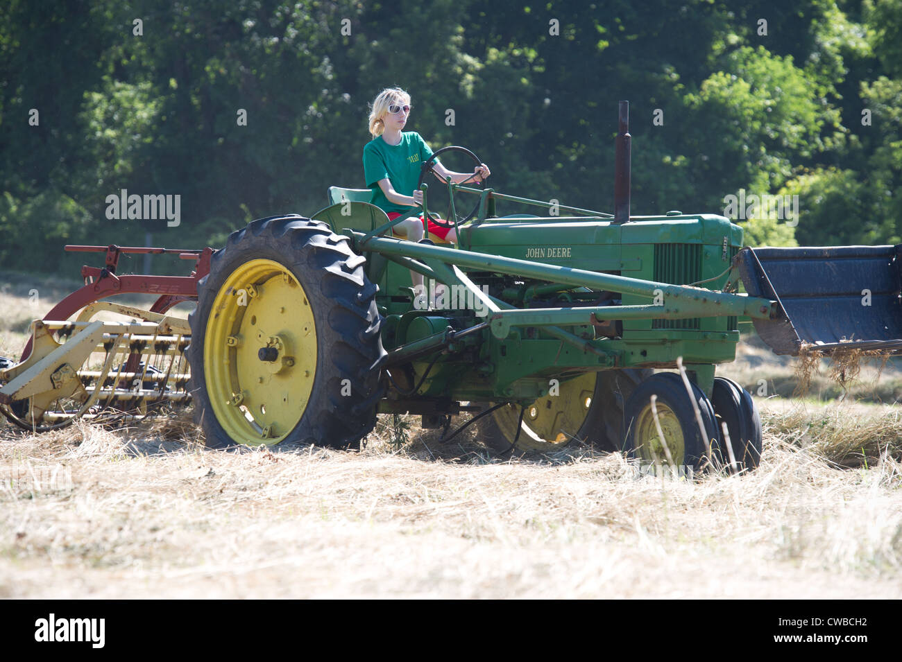 Ragazza adolescente a rastrellare il fieno con John Deere modello 50 e del trattore New Holland bar rastrello Foto Stock