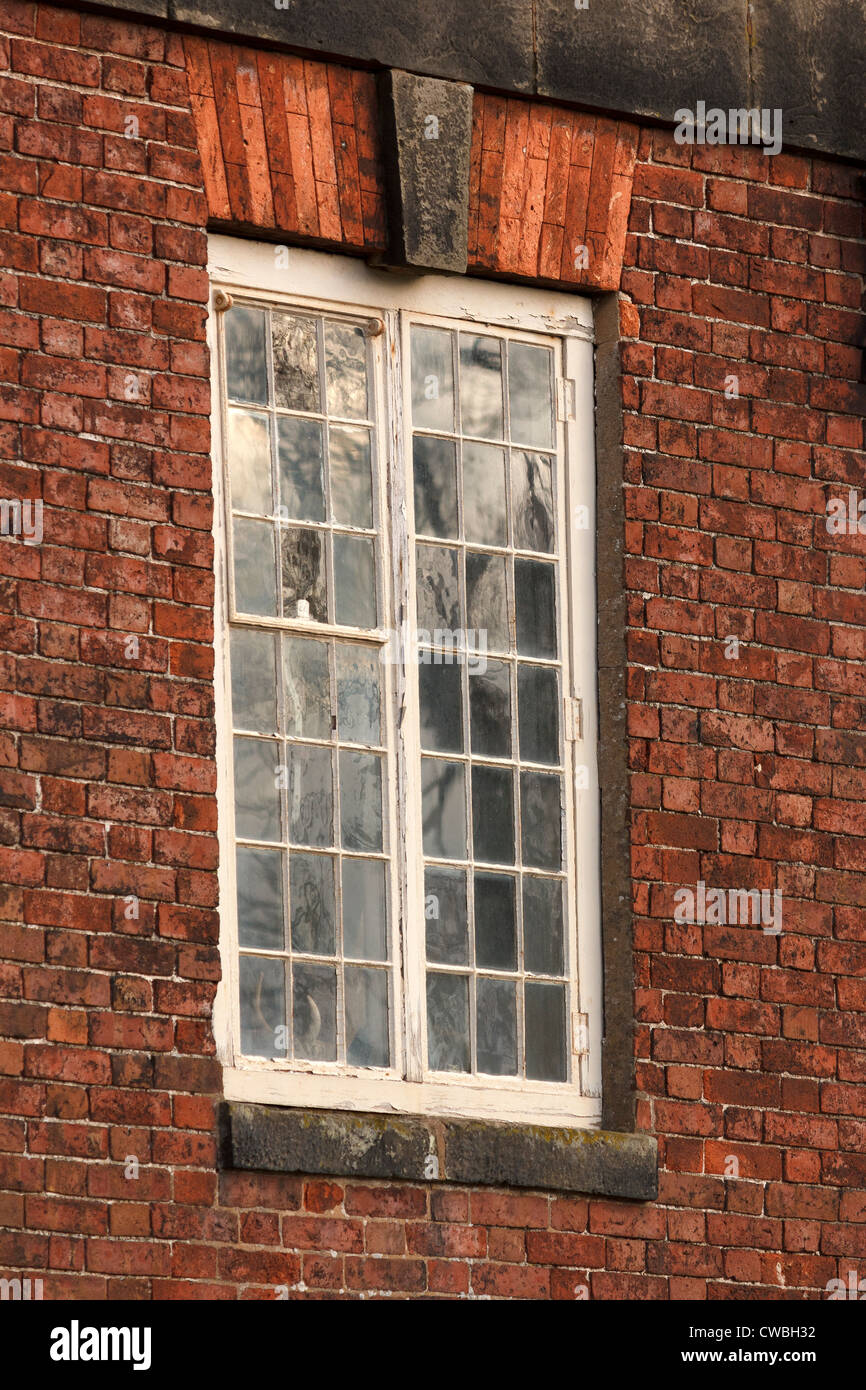 Riflessioni nella vecchia finestra con piccoli riquadri di vetro in rosso un muro di mattoni, Calke Abbey, Ticknall, Derbyshire, England, Regno Unito Foto Stock