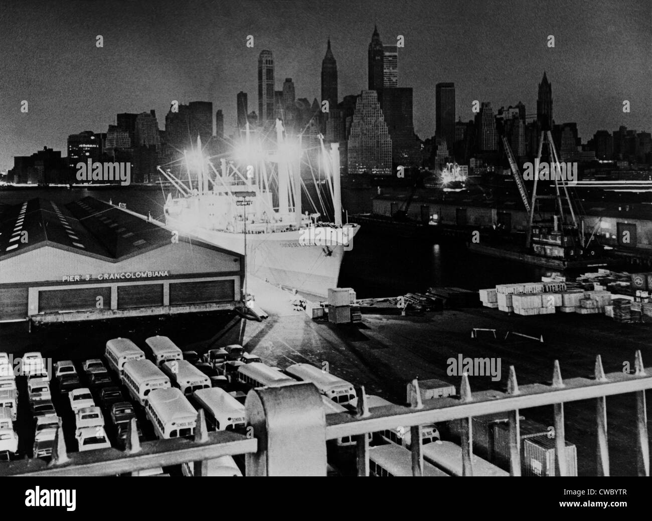 New York Manhattan skyline avvolto nelle tenebre, è compensato dalle luci di un cargo in corrispondenza di un molo di Brooklyn. Su Foto Stock