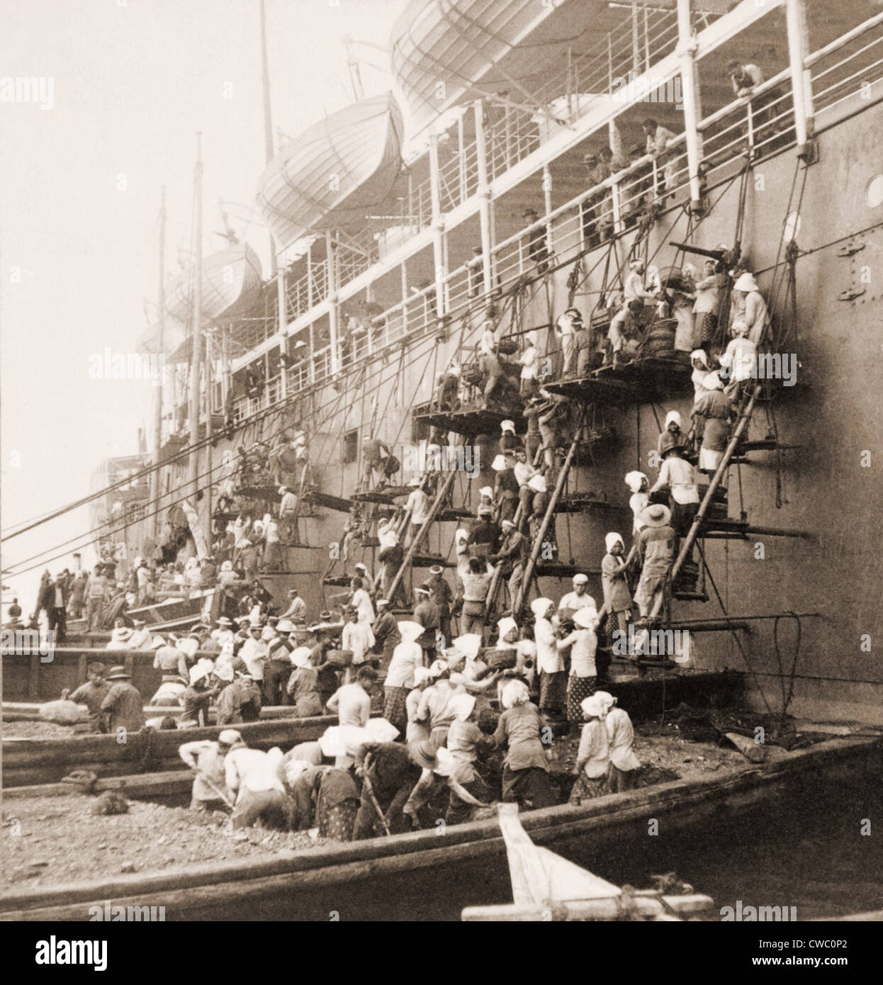 Stazione di rivestimento a Nagasaki, in Giappone. Giovani uomini e donne su chiatte e ponteggi formano una brigata di benna, passando il carbone fino la Foto Stock