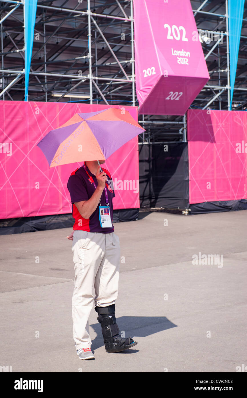 Londra 2012 Stratford Olympic Park volontario membro dello staff giochi Maker parasol ombrello della gamba in nero ortesi piede boot Foto Stock
