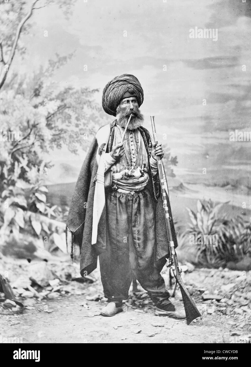 Costantinopoli. La Caldea - Uomo nel tradizionale costume Turco, poste davanti a uno sfondo, tenendo fucile e fumare una tubazione, 1869 Foto Stock