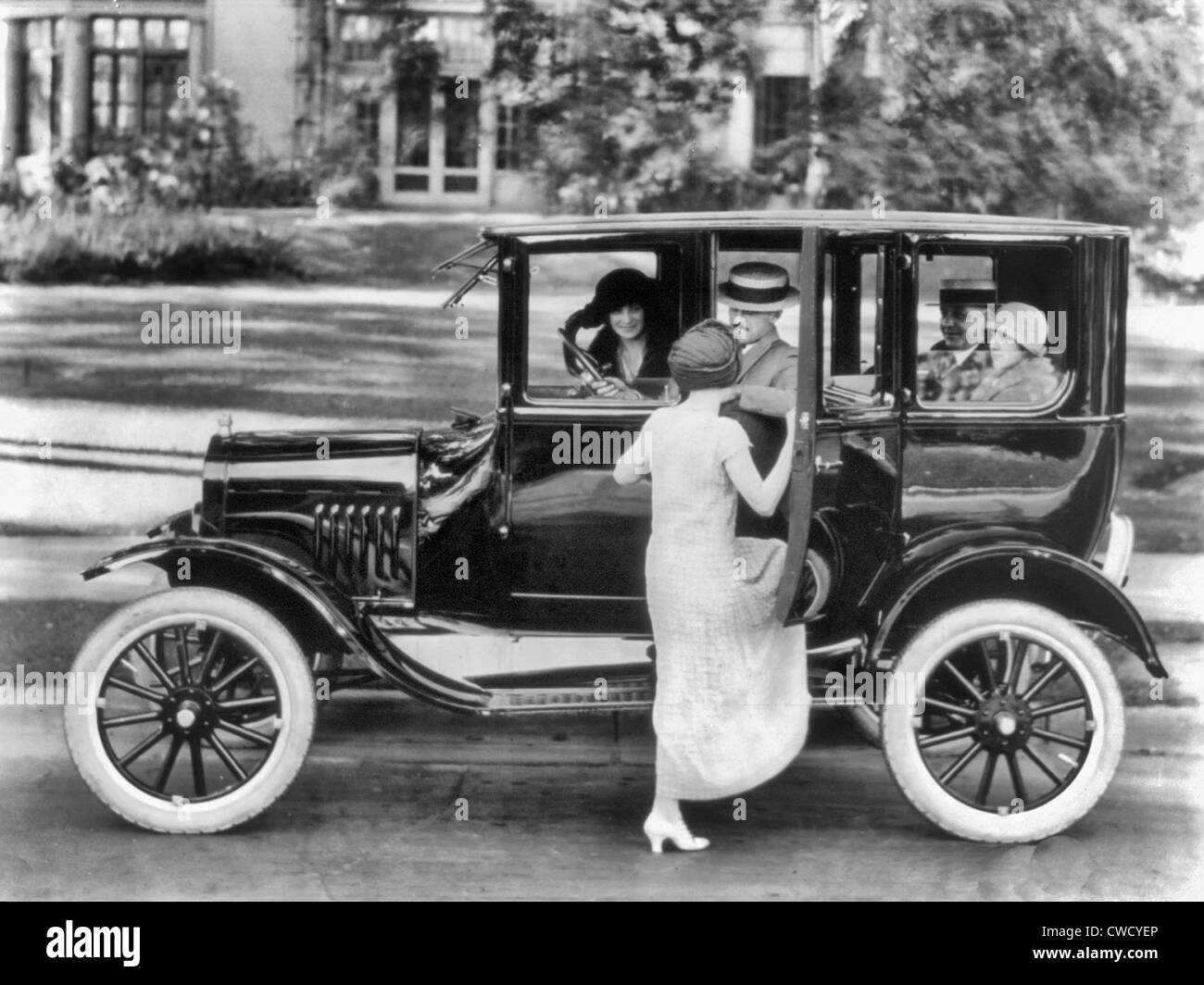 Vista laterale di una Ford berlina con quattro passeggeri e una donna arrivare sul lato conducente, circa 1923 Foto Stock