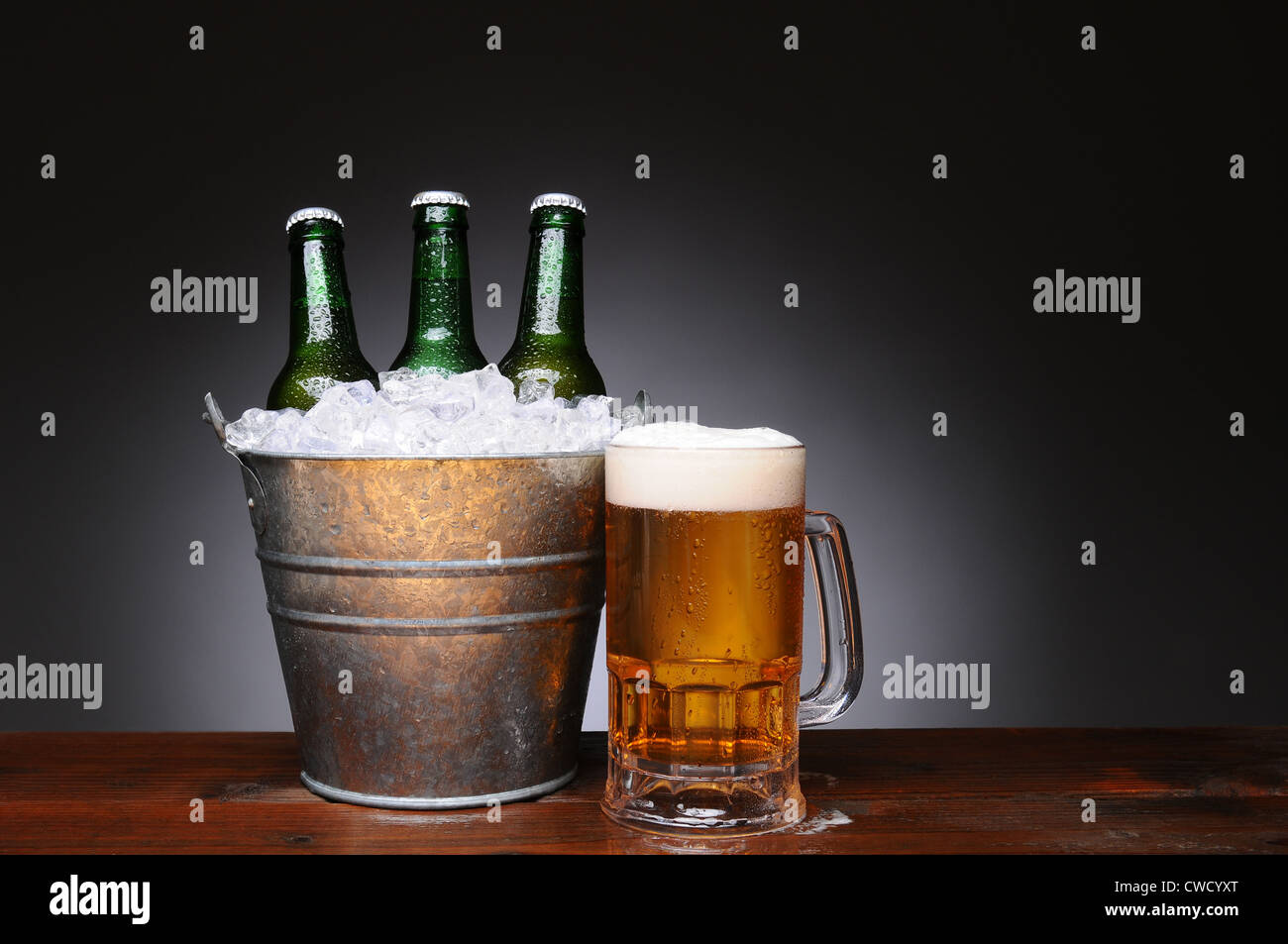 Un secchiello per il ghiaccio con verde tre bottiglie di birra accanto a una tazza piena di ale sul bagnato la superficie di legno. Foto Stock