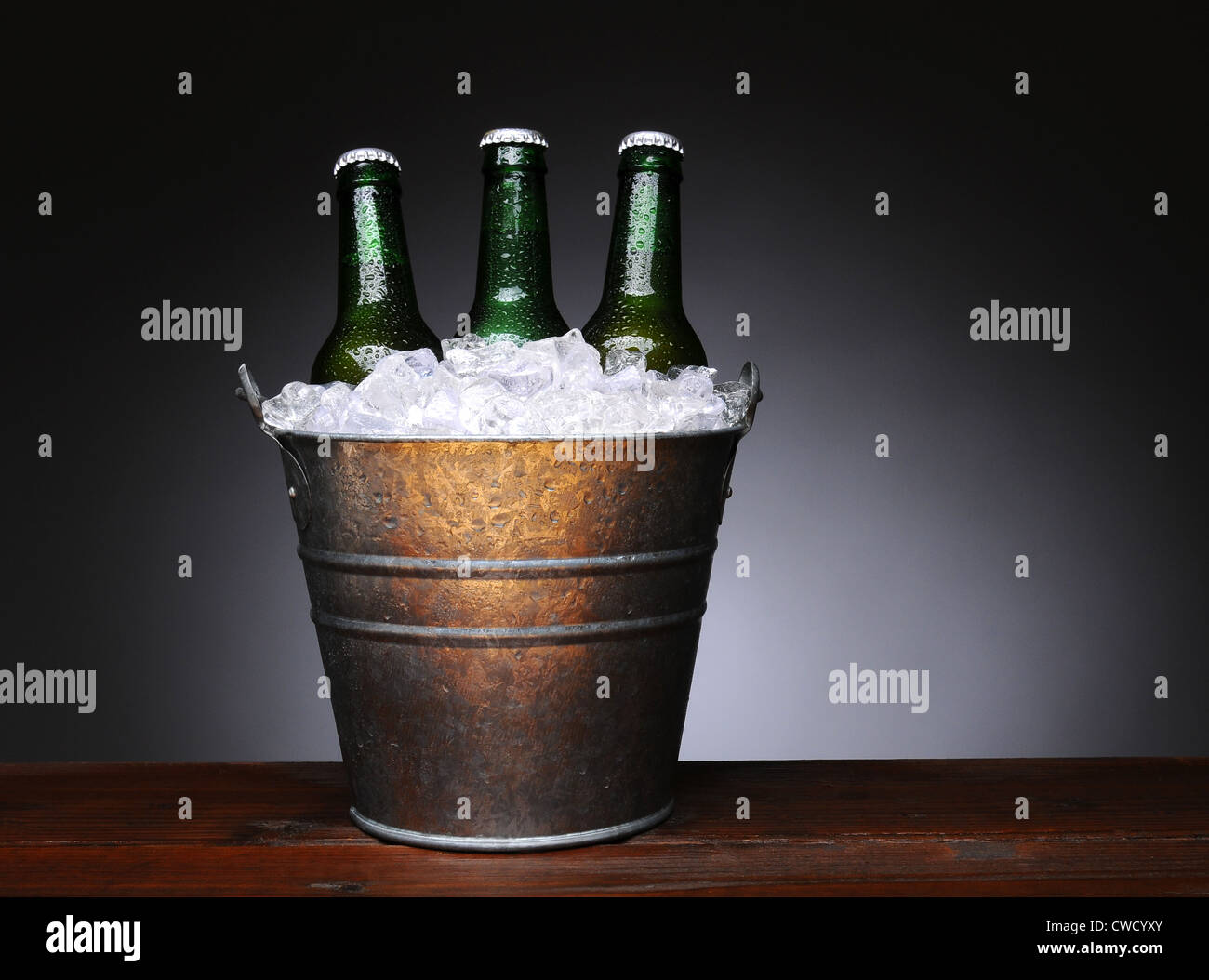Un secchiello per il ghiaccio con verde tre bottiglie di birra su di un legno bagnato superficie. Formato orizzontale con una luce a sfondo grigio scuro. Foto Stock