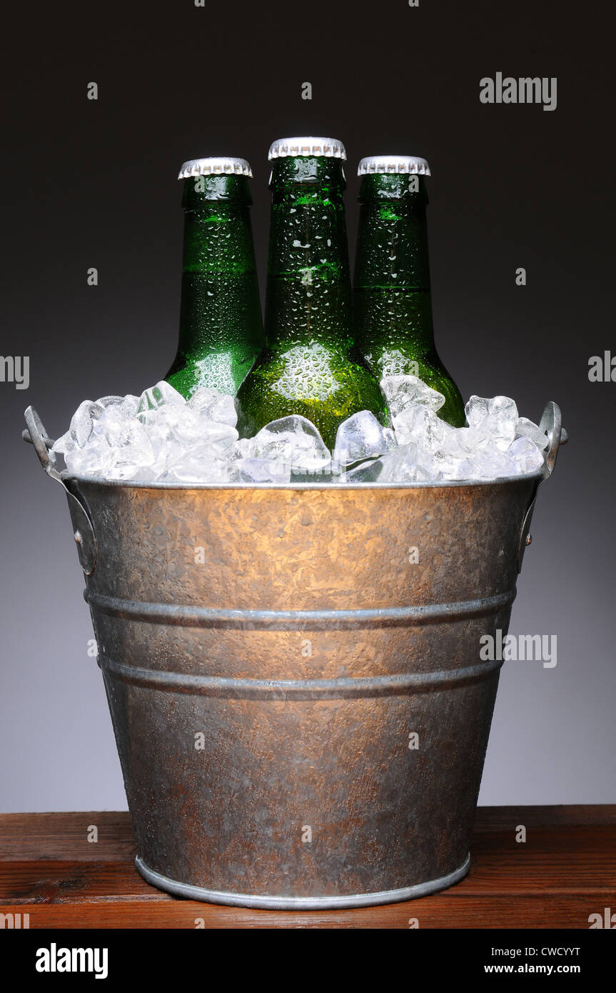 Secchiello per ghiaccio con tre bottiglie di birra su un wet bar in legno sul bancone. Formato verticale su una luce di sfondo grigio scuro. Foto Stock