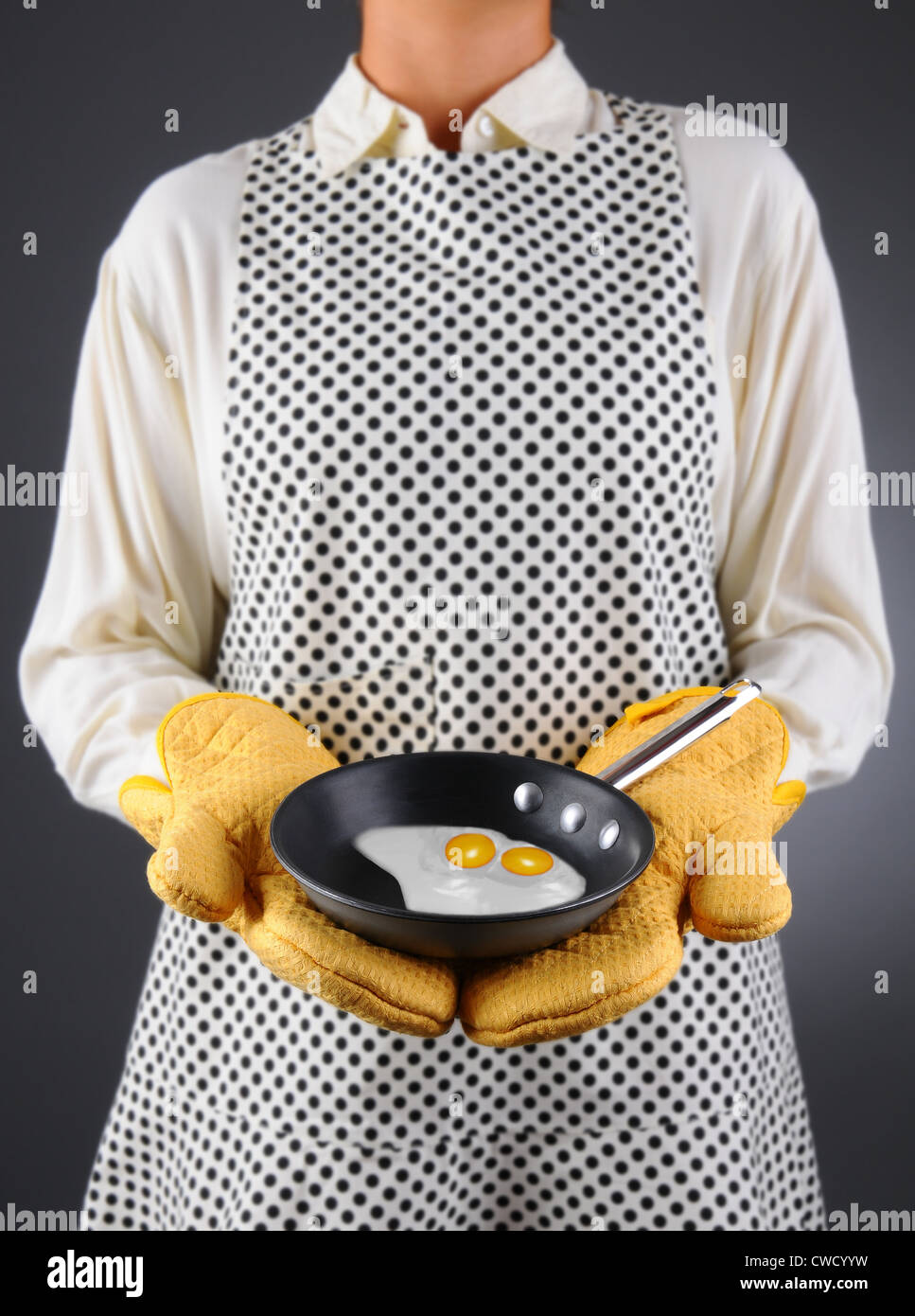 Primo piano di una massaia in un grembiule e guanti da forno tenendo un piattino con due uova fritte. Foto Stock