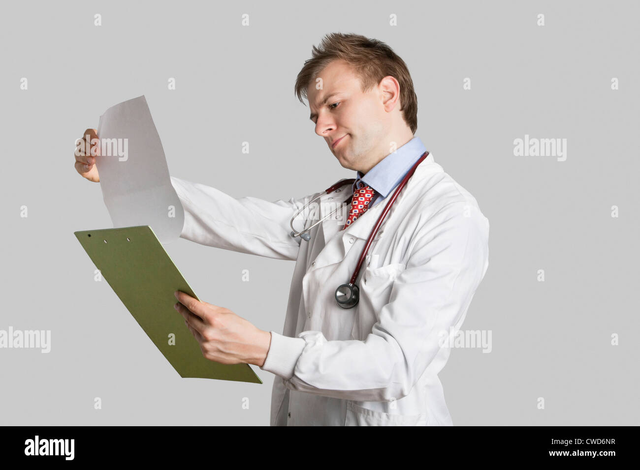 Medico maschio in un camice di lettura record medici su sfondo grigio Foto Stock