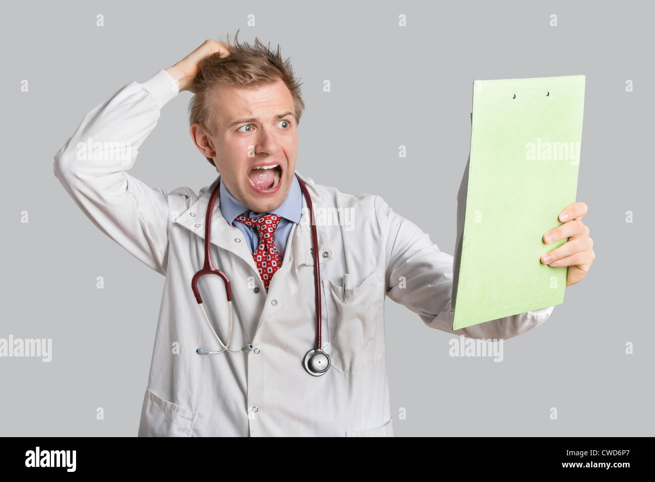 Medico maschio terrorizzato guardando i rapporti medici su sfondo grigio Foto Stock