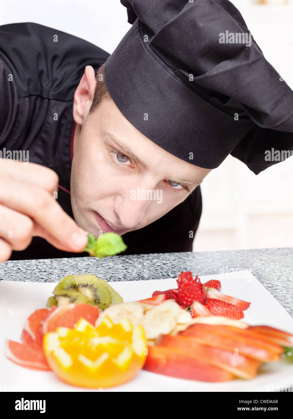 Chef in nero uniforme di decorare delizioso piatto di frutta Foto Stock