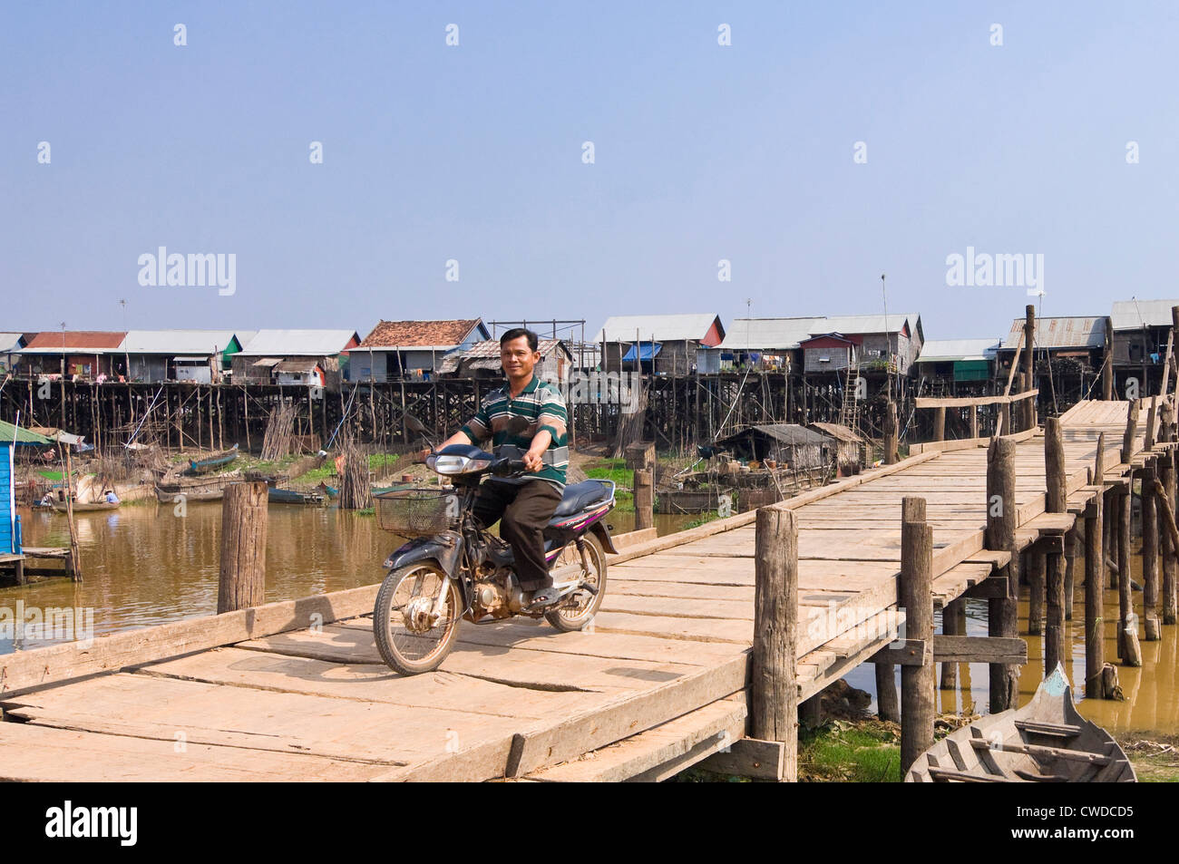 Vista orizzontale di un uomo alla guida di un ciclomotore attraverso un malsicuro vecchio ponte di Kompong Khleang villaggio galleggiante, in Cambogia. Foto Stock