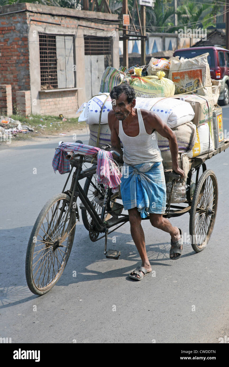 L'uomo spingendo pesantemente caricato di risciò ciclo attraverso le strade di Baruipur, West Bengal, India, 13 gennaio 2009. Foto Stock