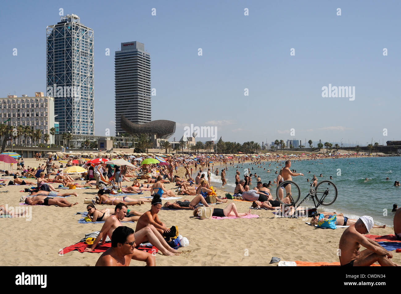 La gente sulla spiaggia di Barceloneta sullo sfondo dell'Hotel Arts edificio progettato dall architetto Bruce Graham di grattacieli Skidmore, Foto Stock
