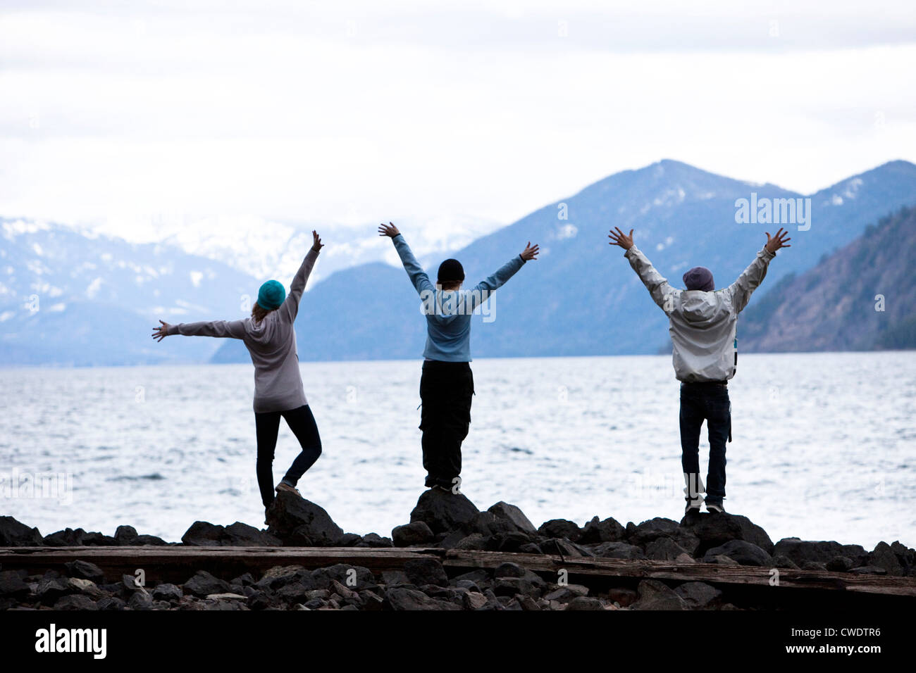 Un gruppo di tre giovani adulti in piedi con le braccia aperte in corrispondenza del bordo di un lago in Idaho. Foto Stock