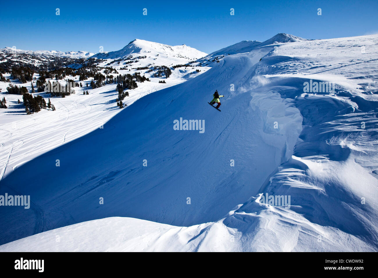 Uno snowboarder salta fuori da un cornicione su una soleggiata giornata invernale in Montana. Foto Stock