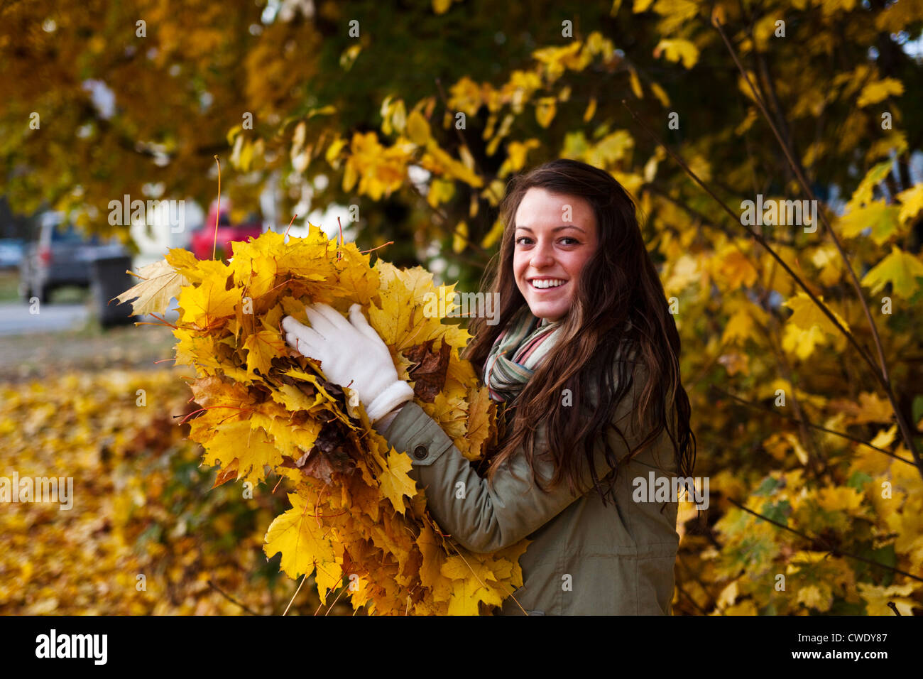 Un atletico giovane donna sorridente tiene un gran mucchio di foglie d'arancio in autunno in Idaho. Foto Stock