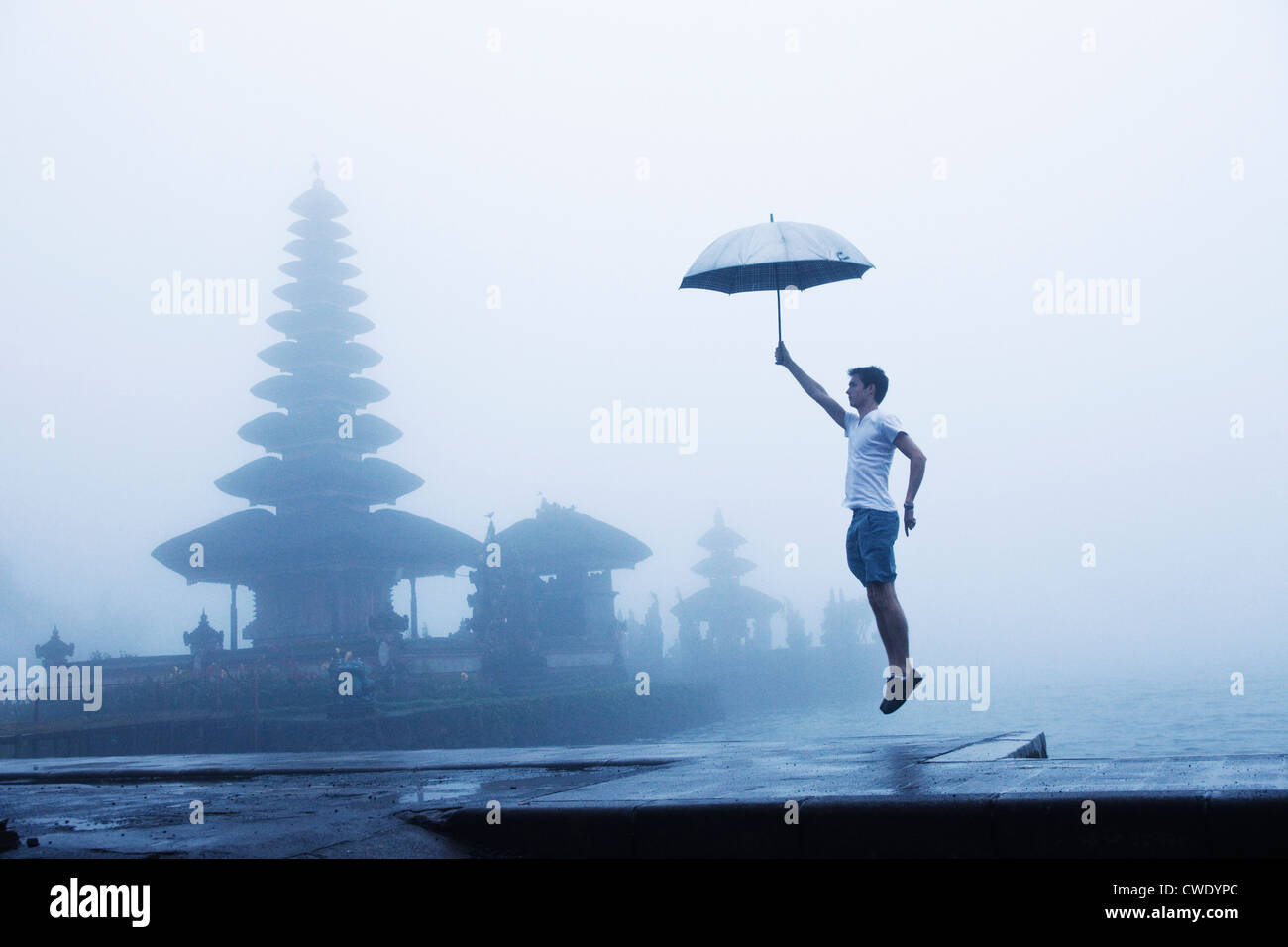 Un uomo salta in aria sui gradini di un tempio con un sfondo velato di Bali, Indonesia. Foto Stock