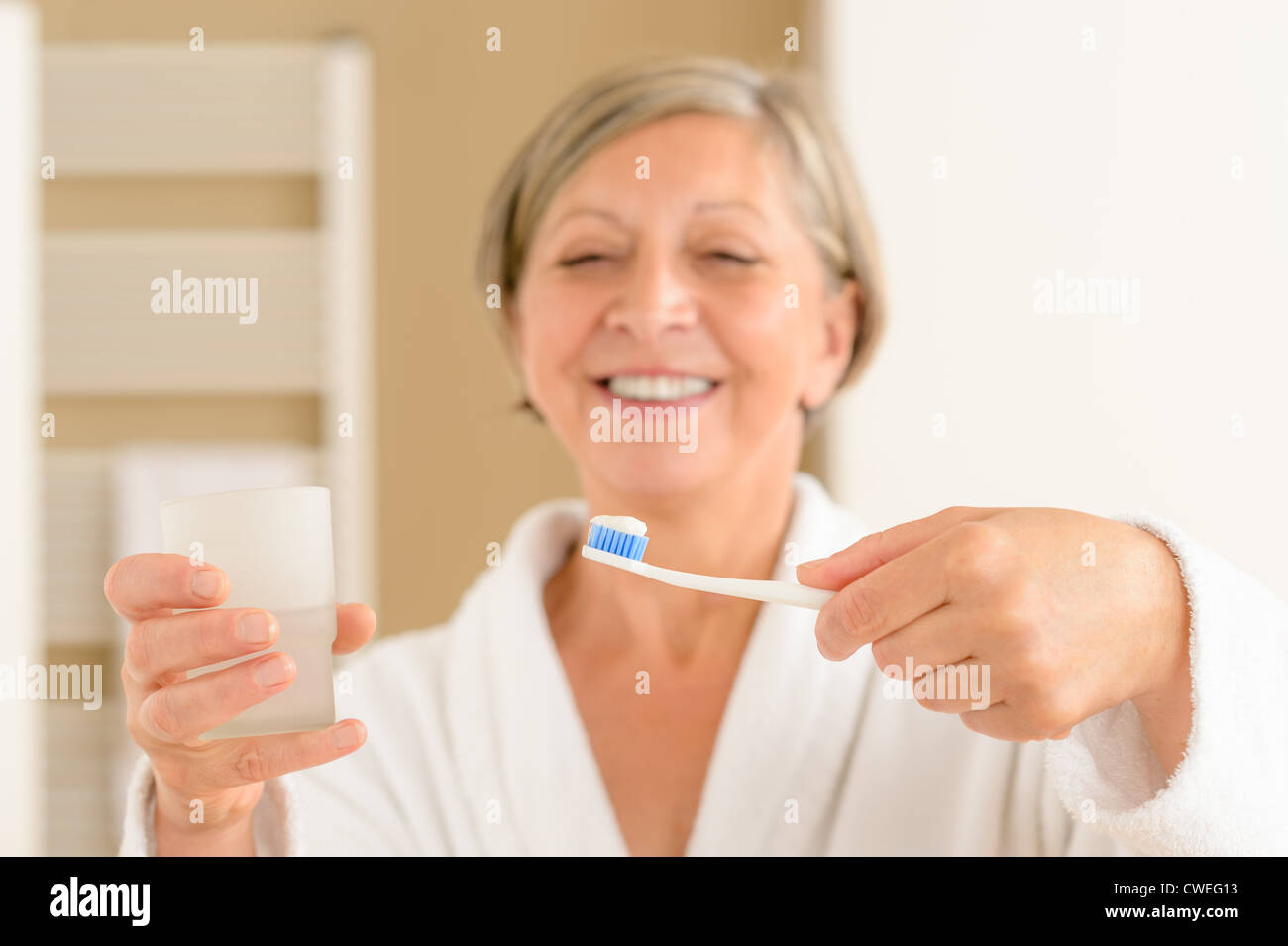 Senior donna tenere uno spazzolino da denti con dentifricio e bicchiere di acqua Foto Stock
