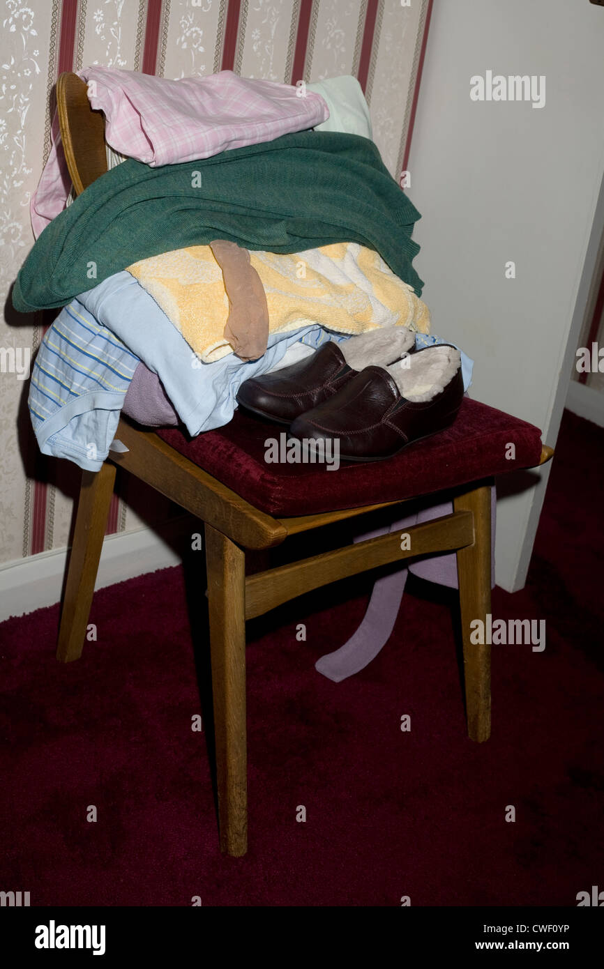 Sedia in camera da letto con pila ordinata di vestiti e pantofole Foto Stock