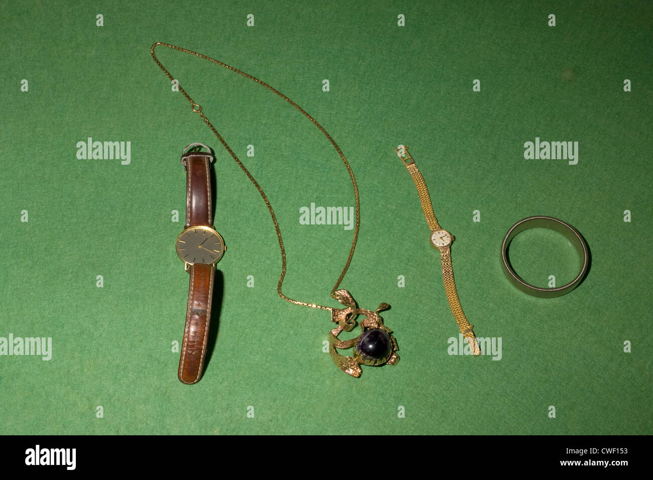 Una raccolta di oggetti di valore con due orologi, una spilla e bangle stabilite per il display sul green baize Foto Stock
