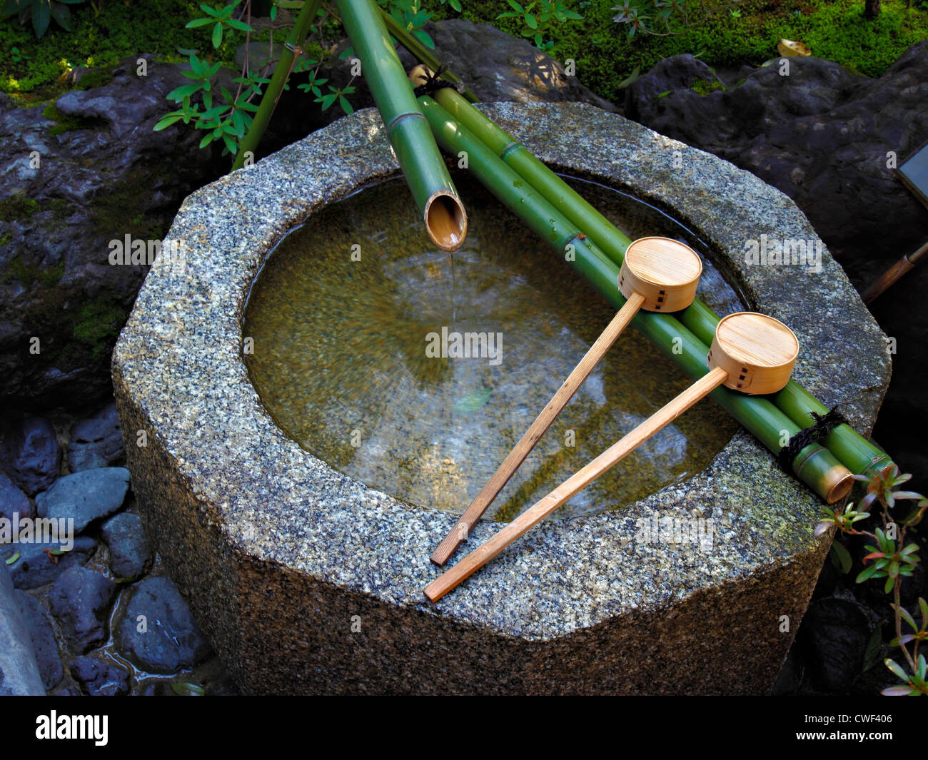 Ottagonale in pietra naturale bacino riempito con acqua dal tubo di bambù con due mestoli di legno Foto Stock