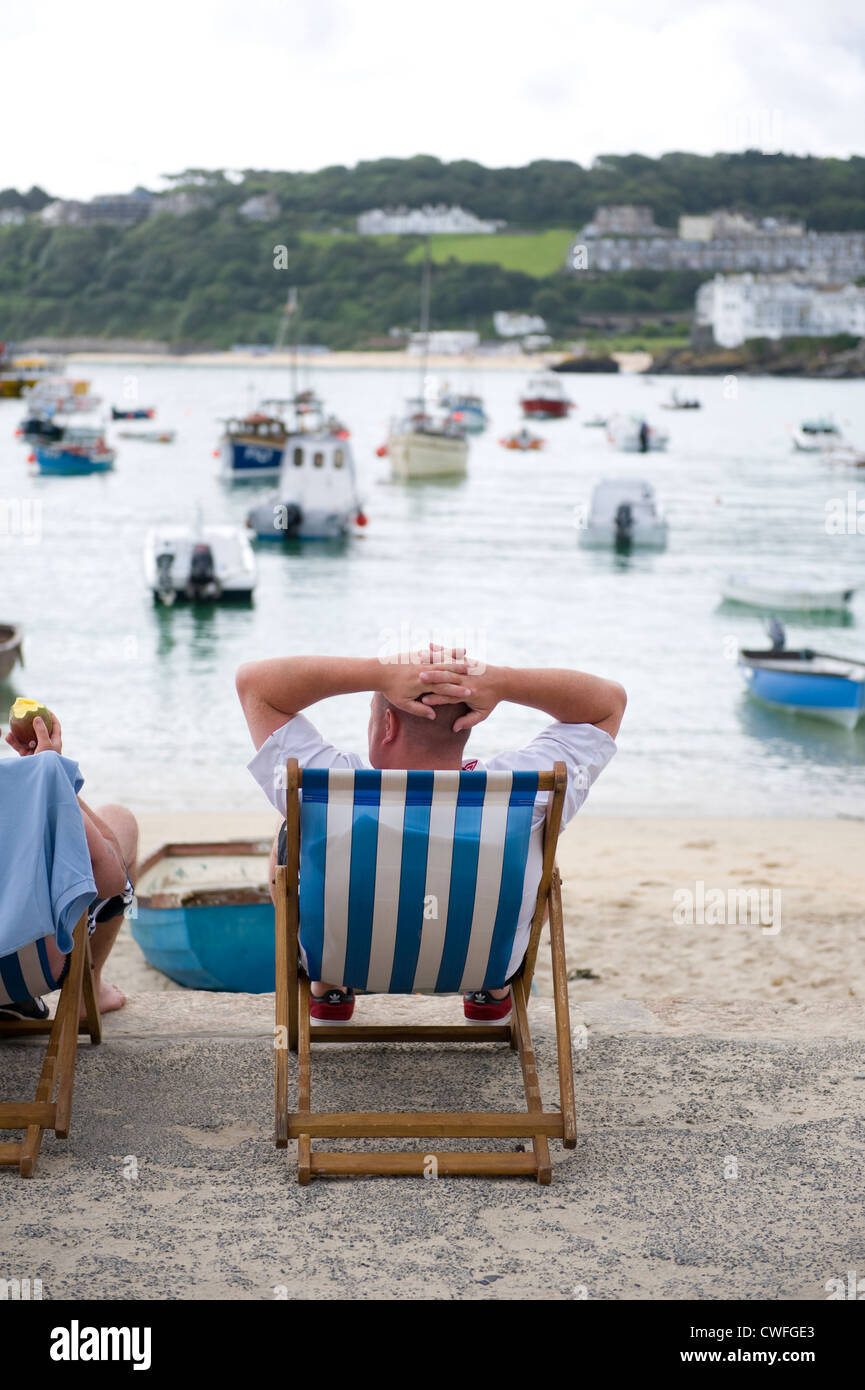 Uomo seduto in una sedia a sdraio presso il porto di St ives cornwall Foto Stock