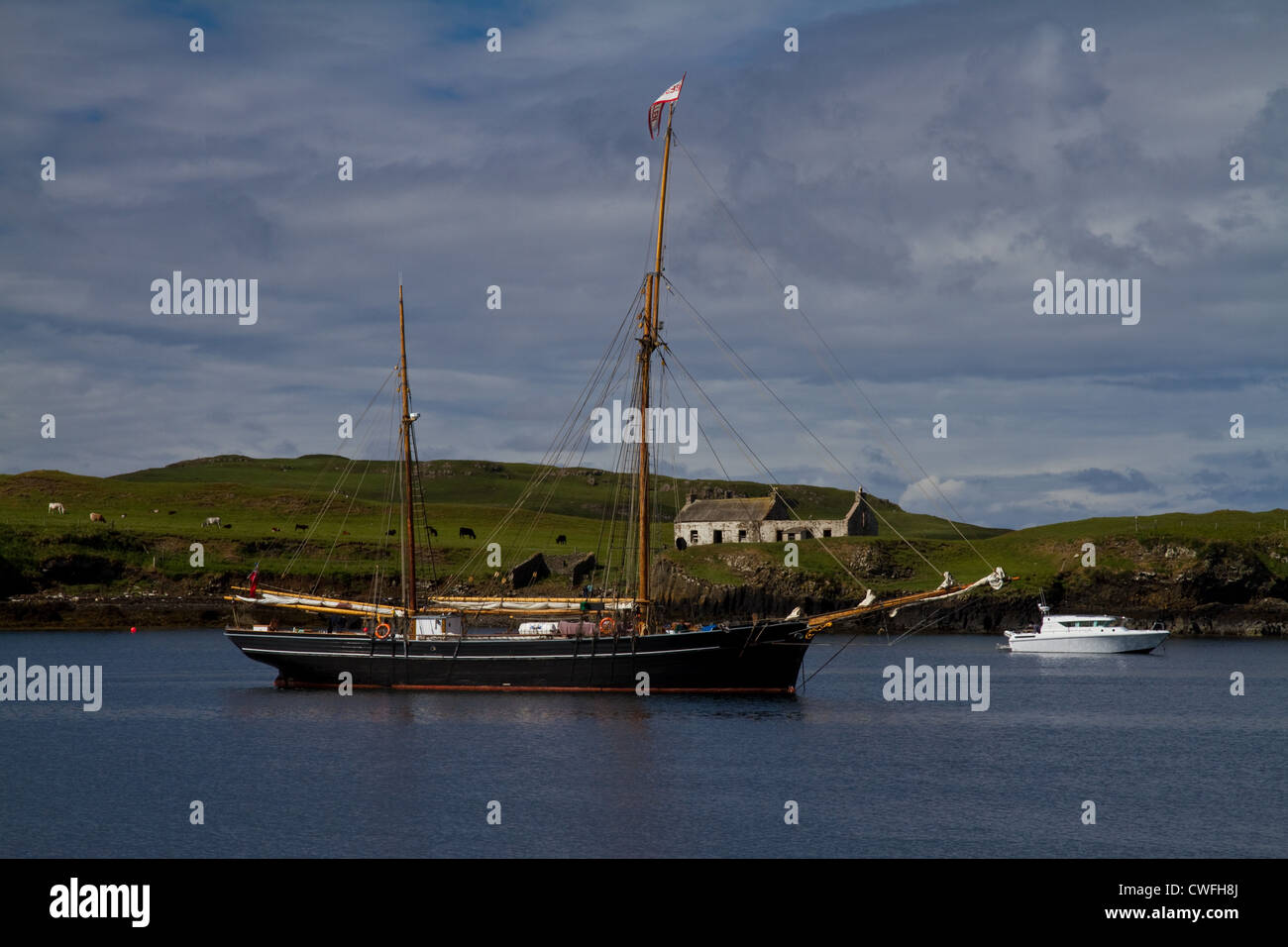 Una barca a vela in legno barca accanto a una moderna imbarcazione a motore nel porto di Canna, piccole isole, con le rovine di Point House dietro Foto Stock