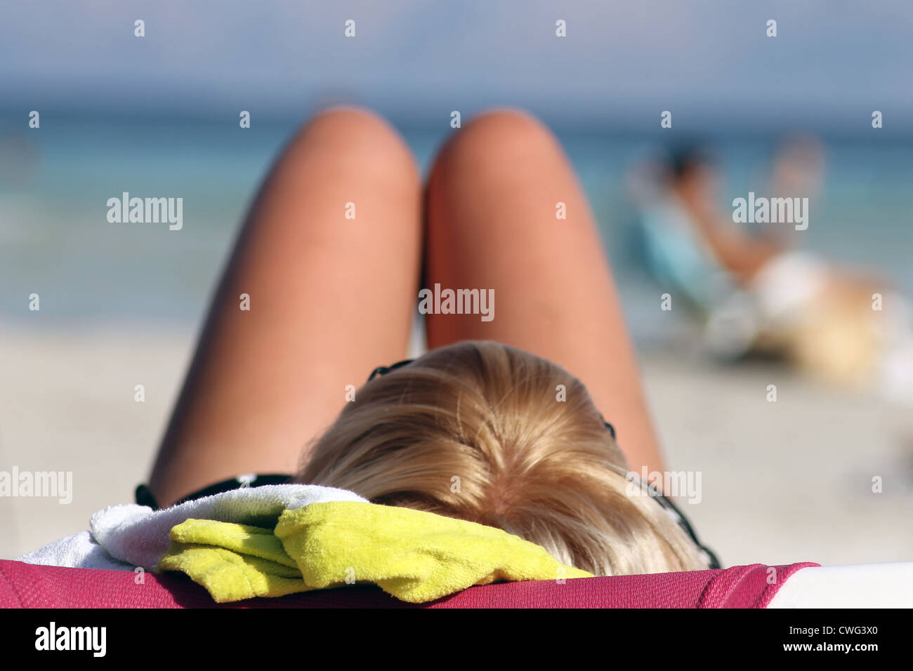 Vista posteriore del giovane donna bionda a prendere il sole sulla spiaggia di sabbia di mare in background. Foto Stock