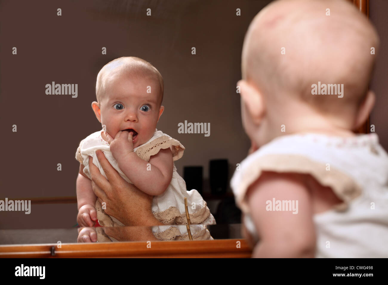 Un bambino di 6 mesi ragazza sorride come essa riconosce se stessa in uno specchio mentre è trattenuto da una mano mans Foto Stock