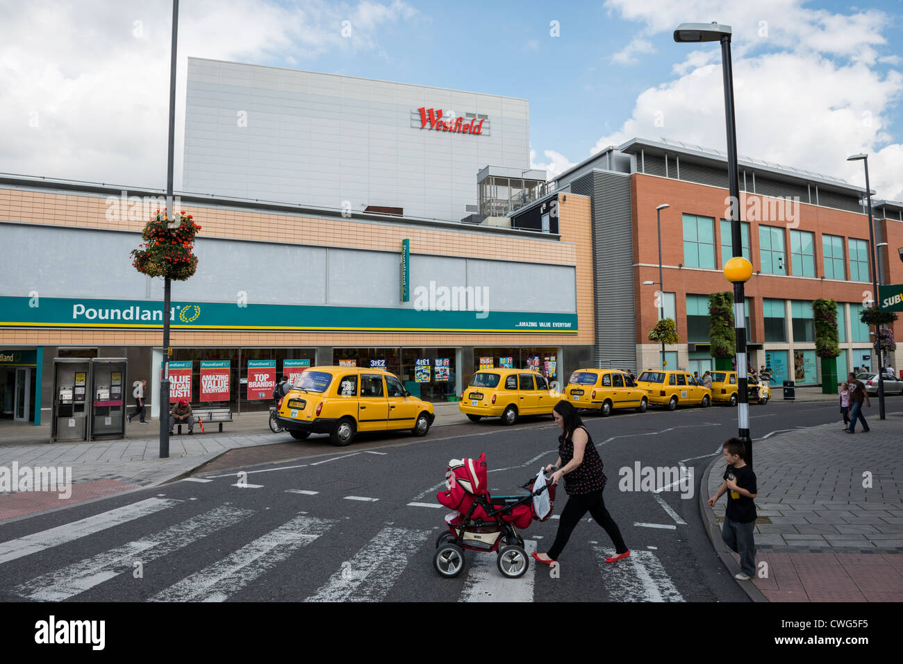 Madre con bambino passeggino spinta attraverso le strisce pedonali nei pressi di servizio taxi fuori Poundland e Westfield in loco Derby Foto Stock